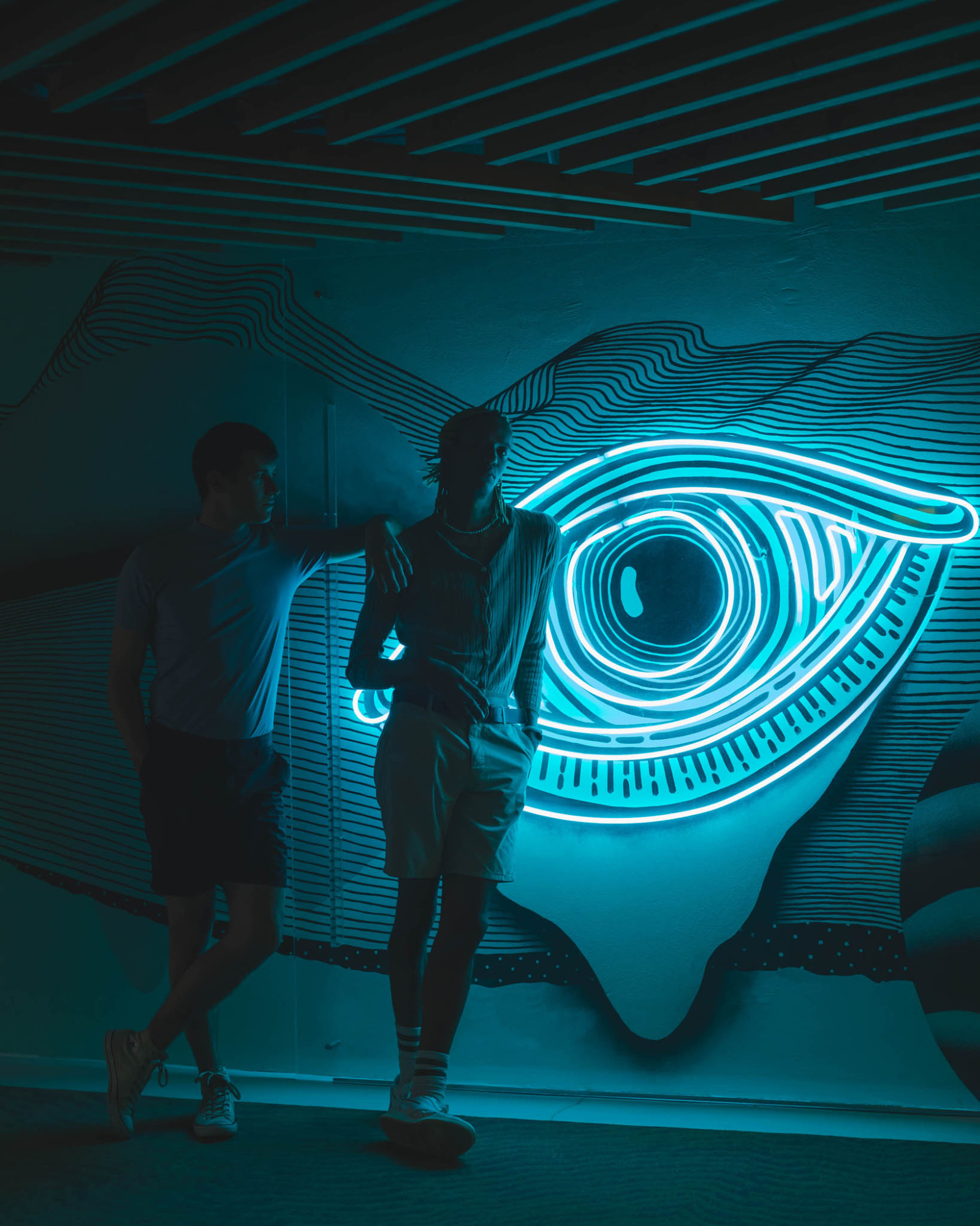 Dos personas caminan por un pasillo con un mural de luces en forma de espiral.