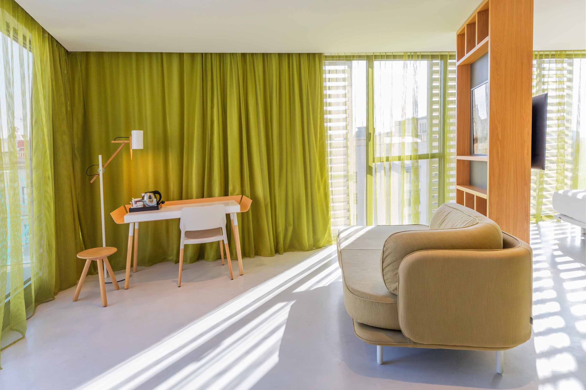 Se ve una habitación con una silla, un escritorio pequeño y una ventana con cortinas verdes.