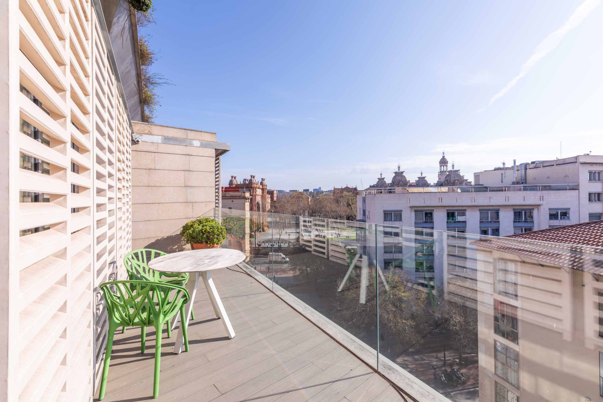 Se ve una terraza con una mesa redonda y sillas junto a una barandilla de vidrio.