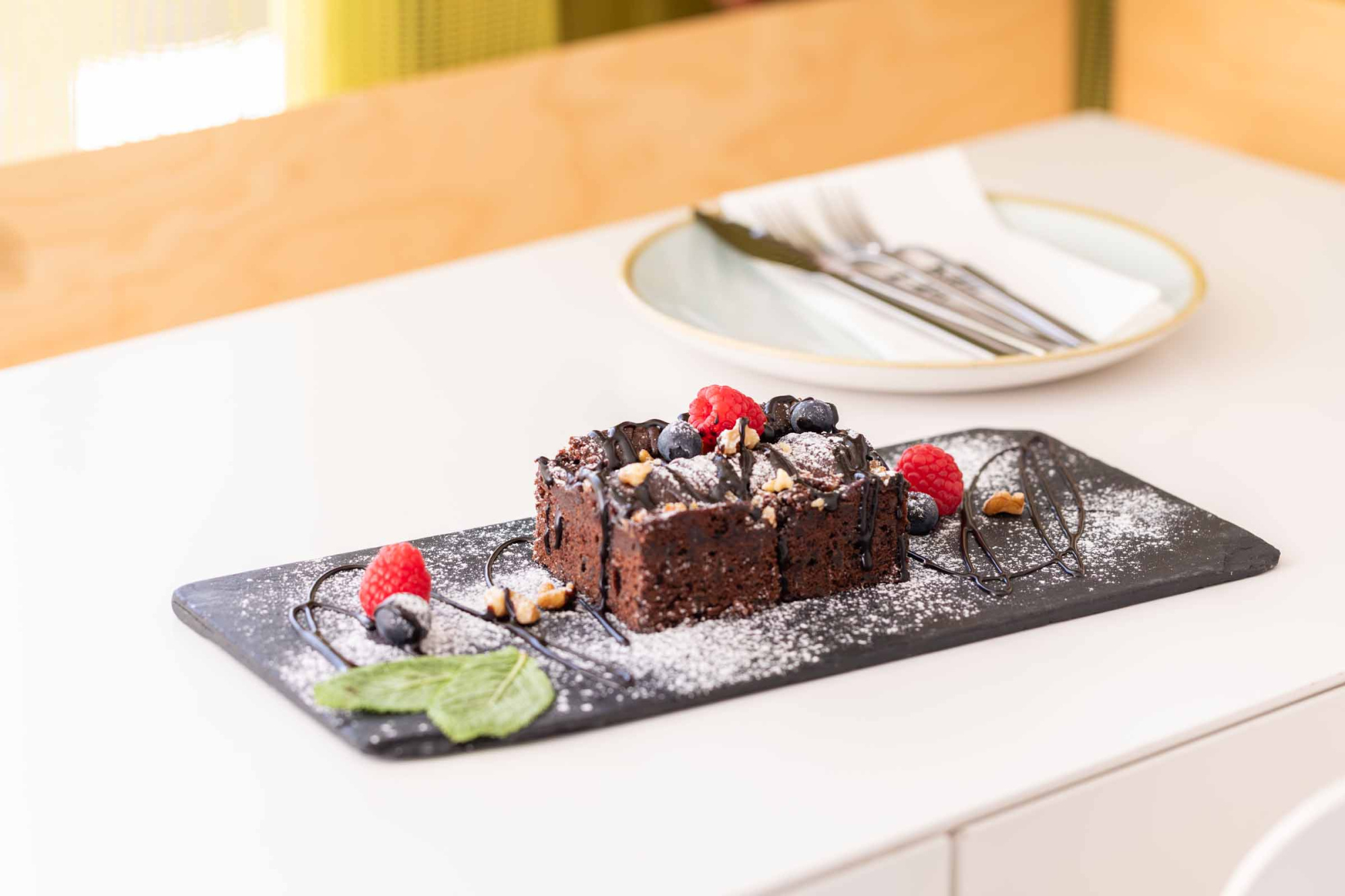 Sirve un postre de chocolate con frutas sobre una bandeja de pizarra en una mesa blanca.