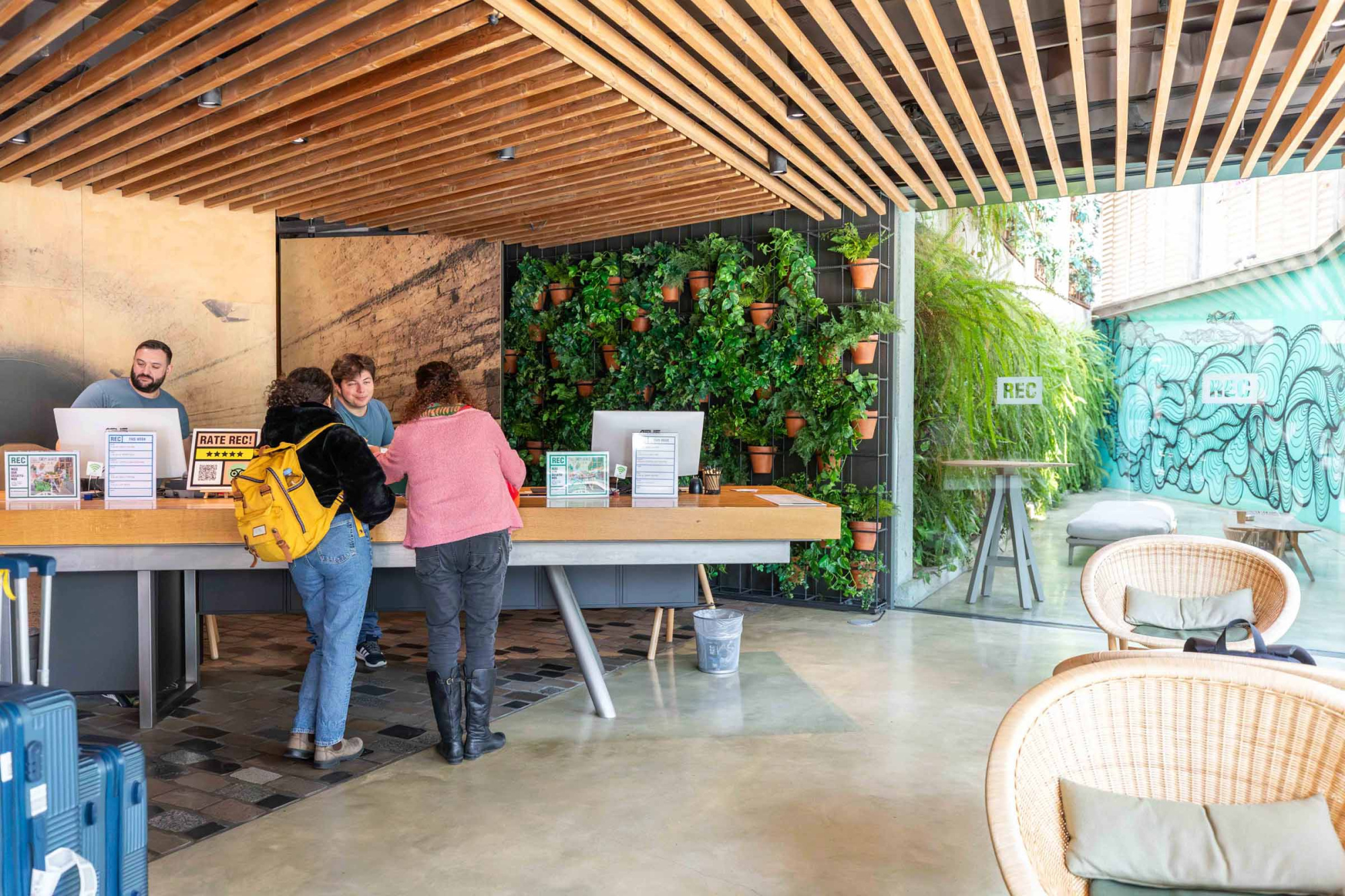 Varias personas conversan en una zona de recepción con mostradores y sillas bajo un techo de madera.