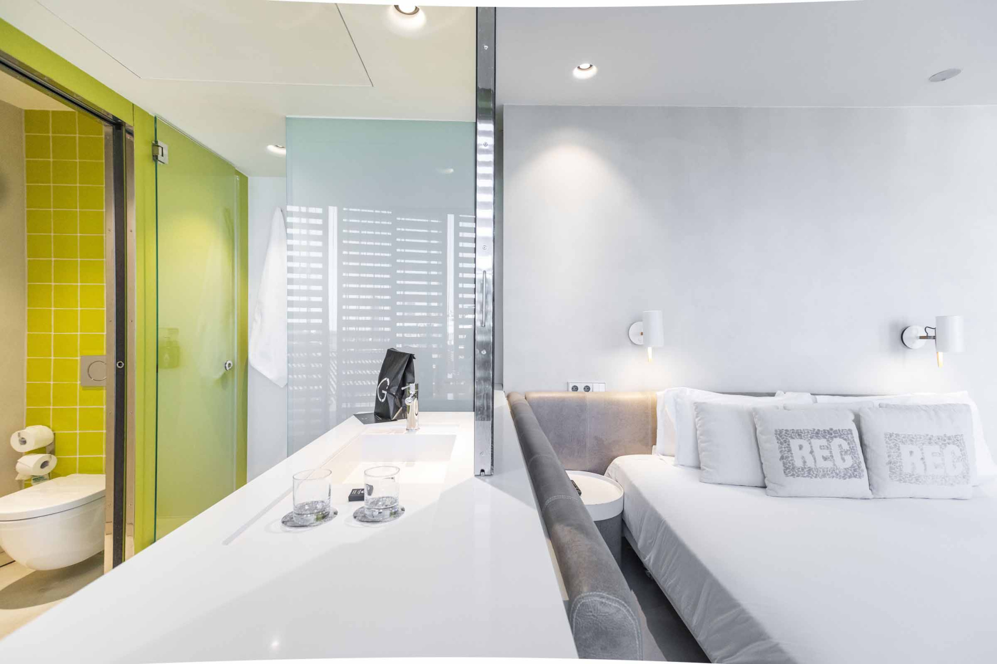 Se ve una bañera blanca junto a una cama con almohadas y una pared gris en el interior.