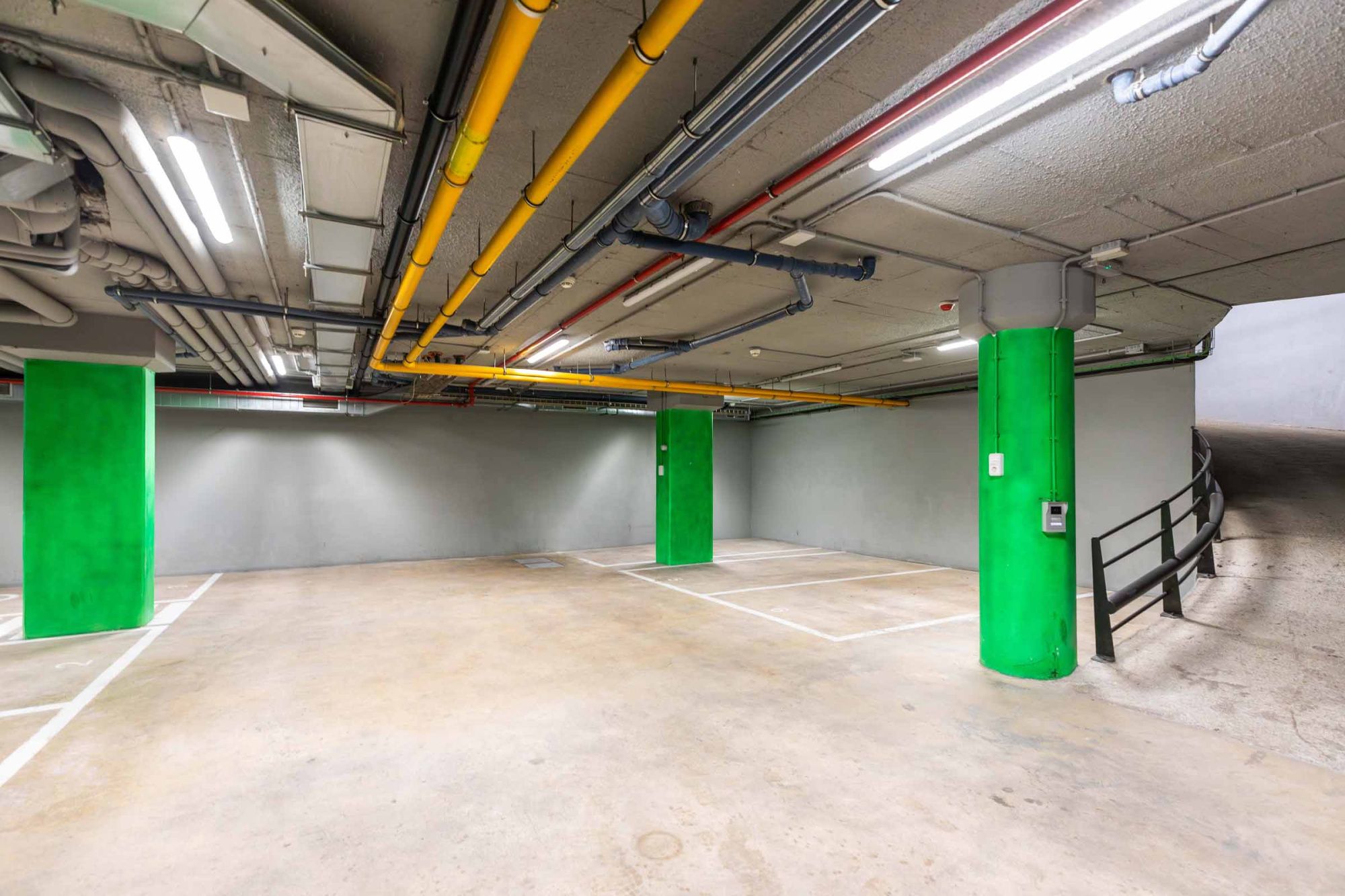 Se ve un garaje con suelo de cemento, pilares verdes y tuberías en el techo.