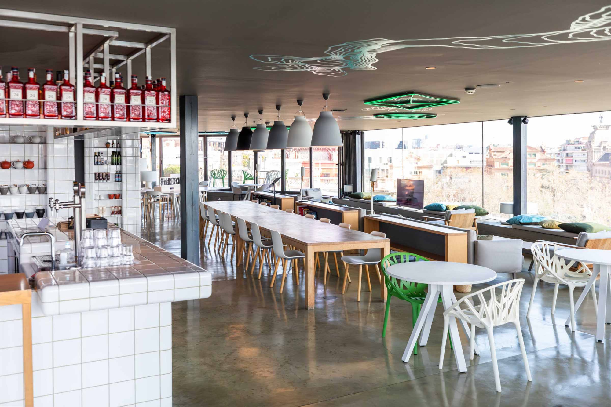 Se ve una zona de bar con taburetes blancos, botellas en estanterías y una barra blanca.