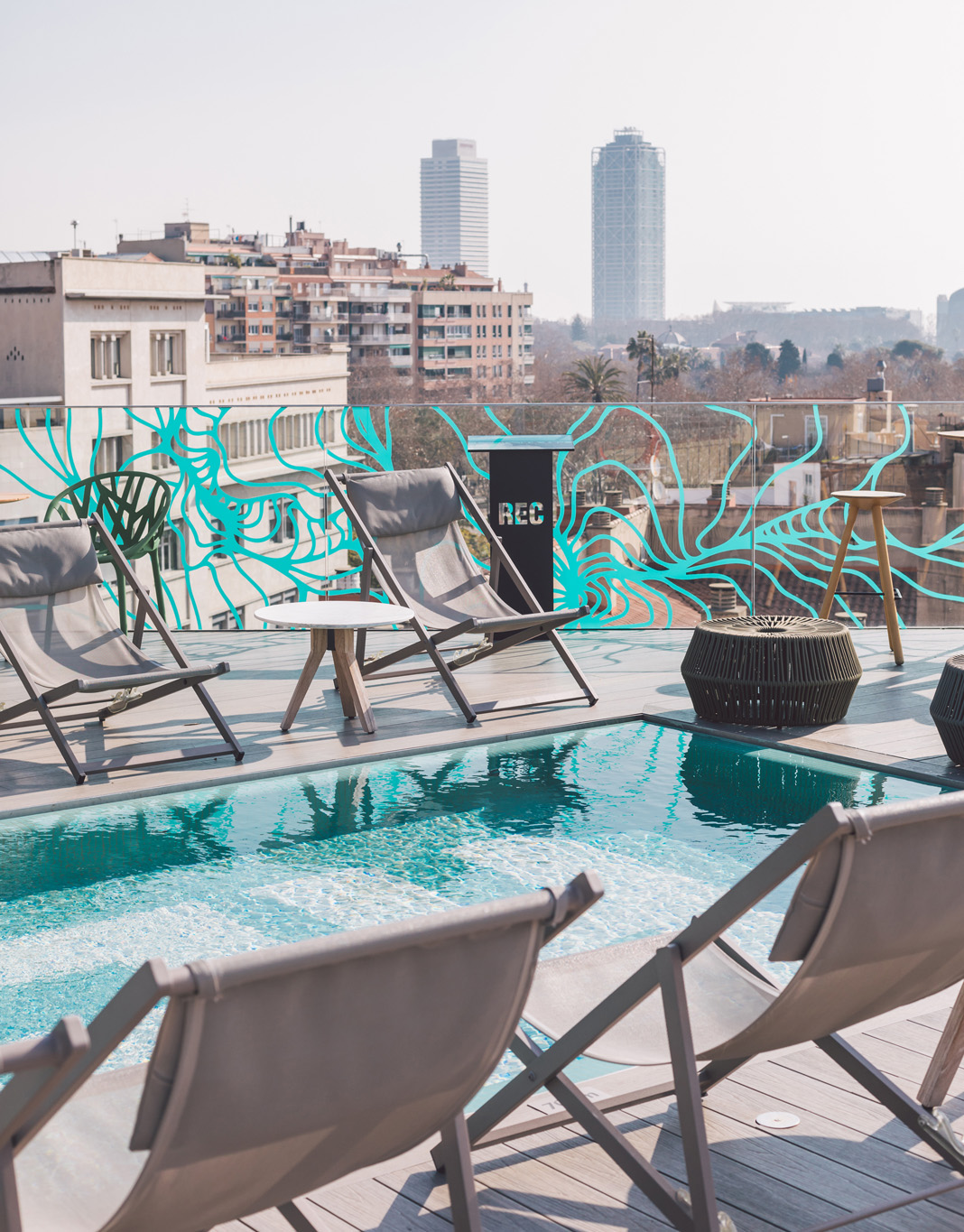 Se ve una terraza con sillas junto a una piscina y una vista urbana al fondo.