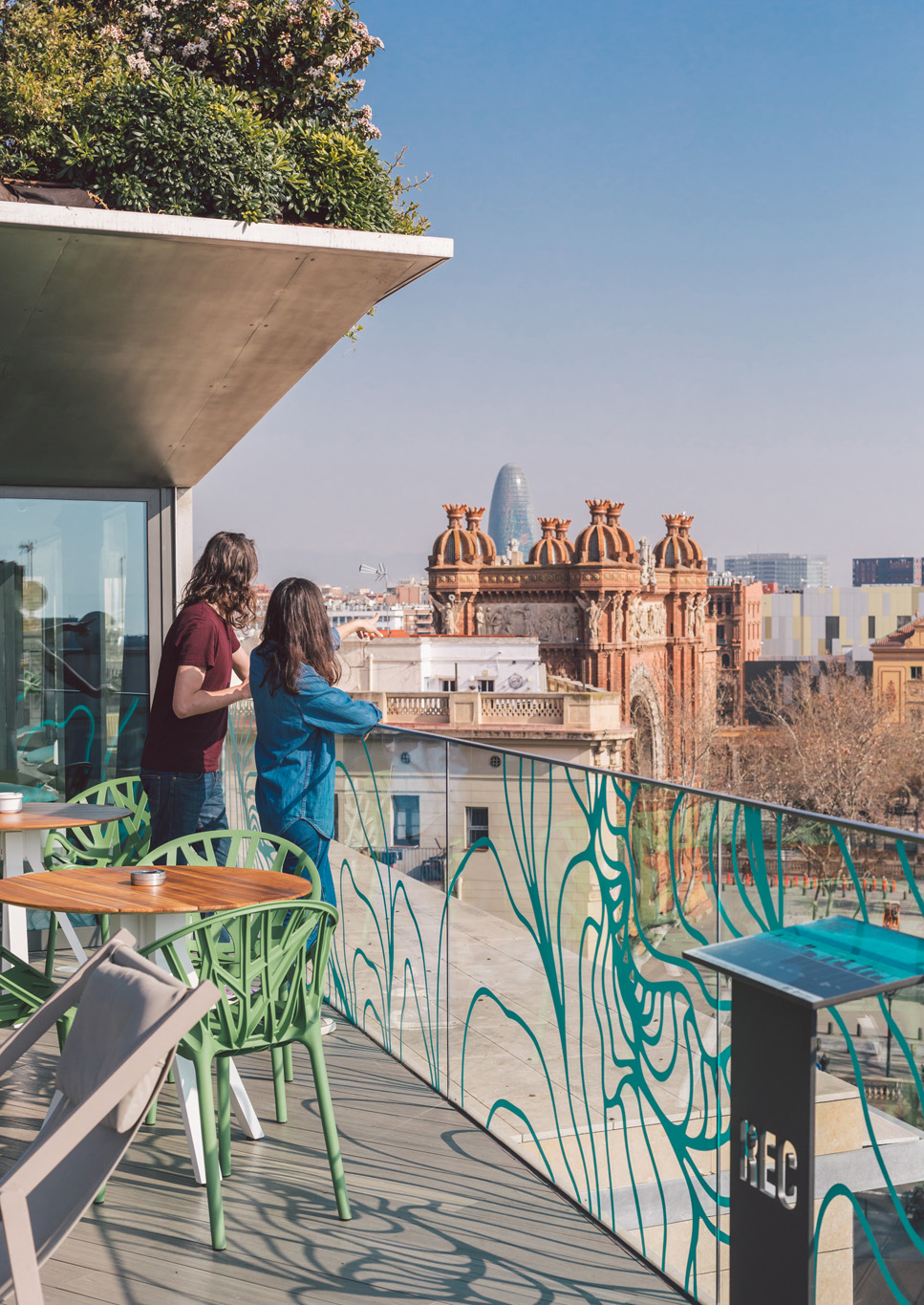 Se ve una terraza con dos sillas de madera, una mesa y una barandilla decorada junto a una piscina al aire libre.