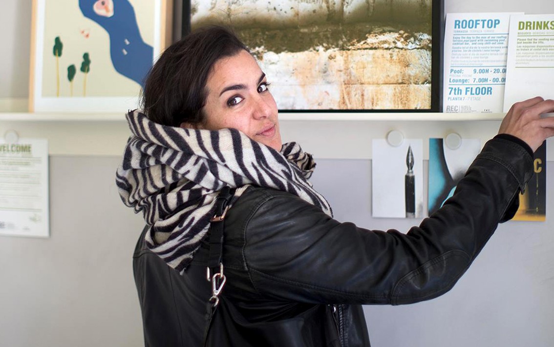 Una recepcionista atiende en un mostrador con un cartel de información detrás.