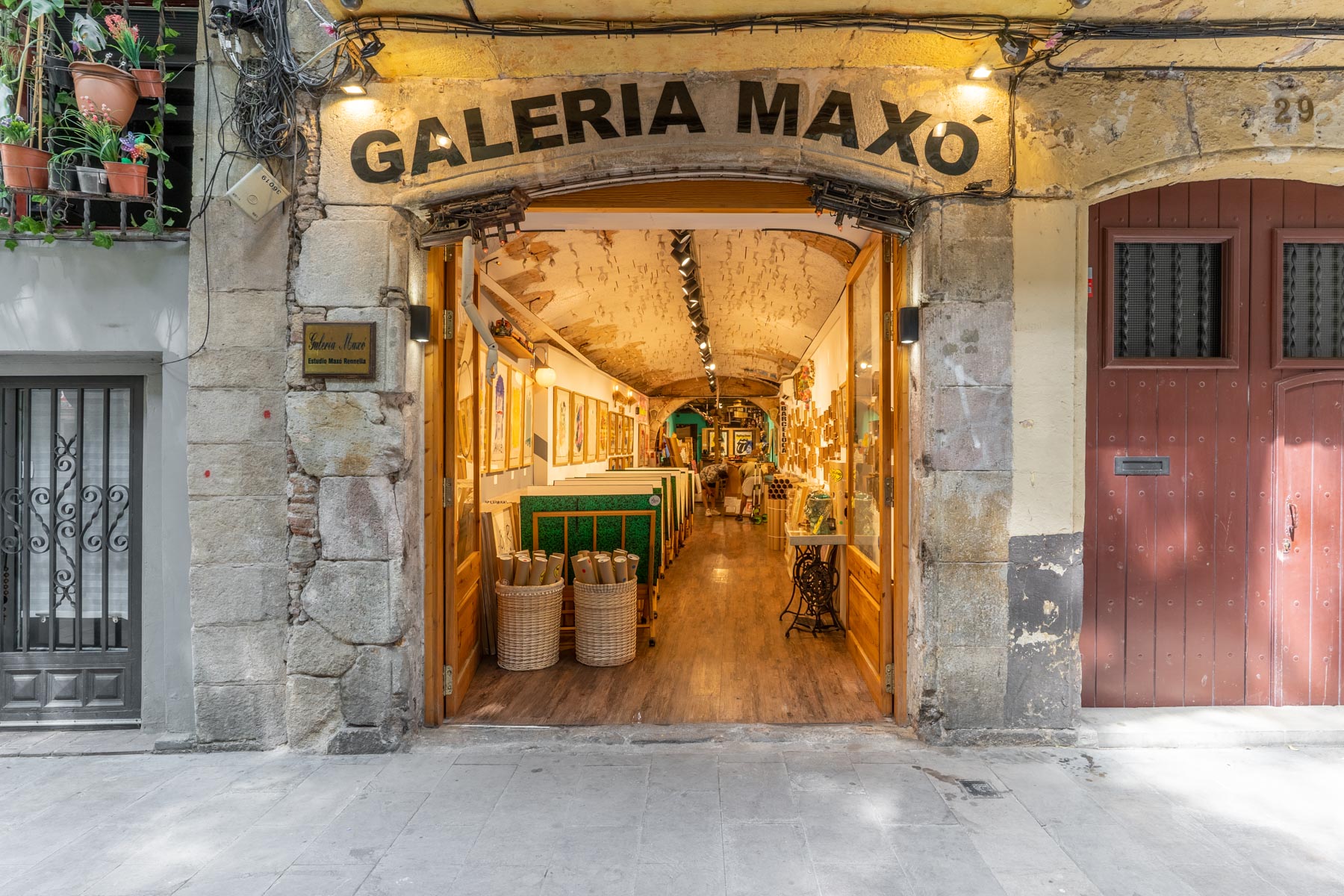 Se ve la entrada de una galería con letrero “GALErIA MAXO” y un pasillo interior con mesas y sillas.