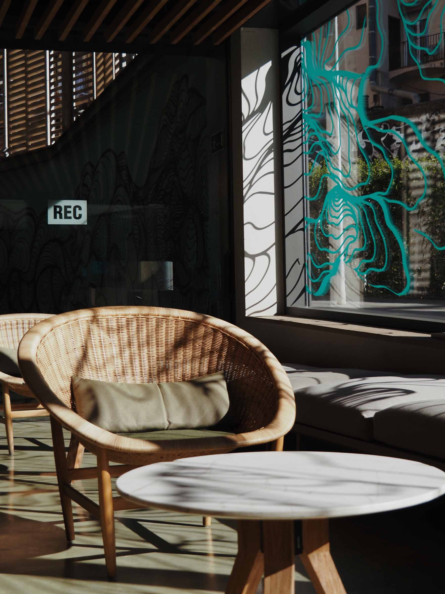 Se ve un sillón de mimbre y una mesa redonda en una terraza con luz natural.