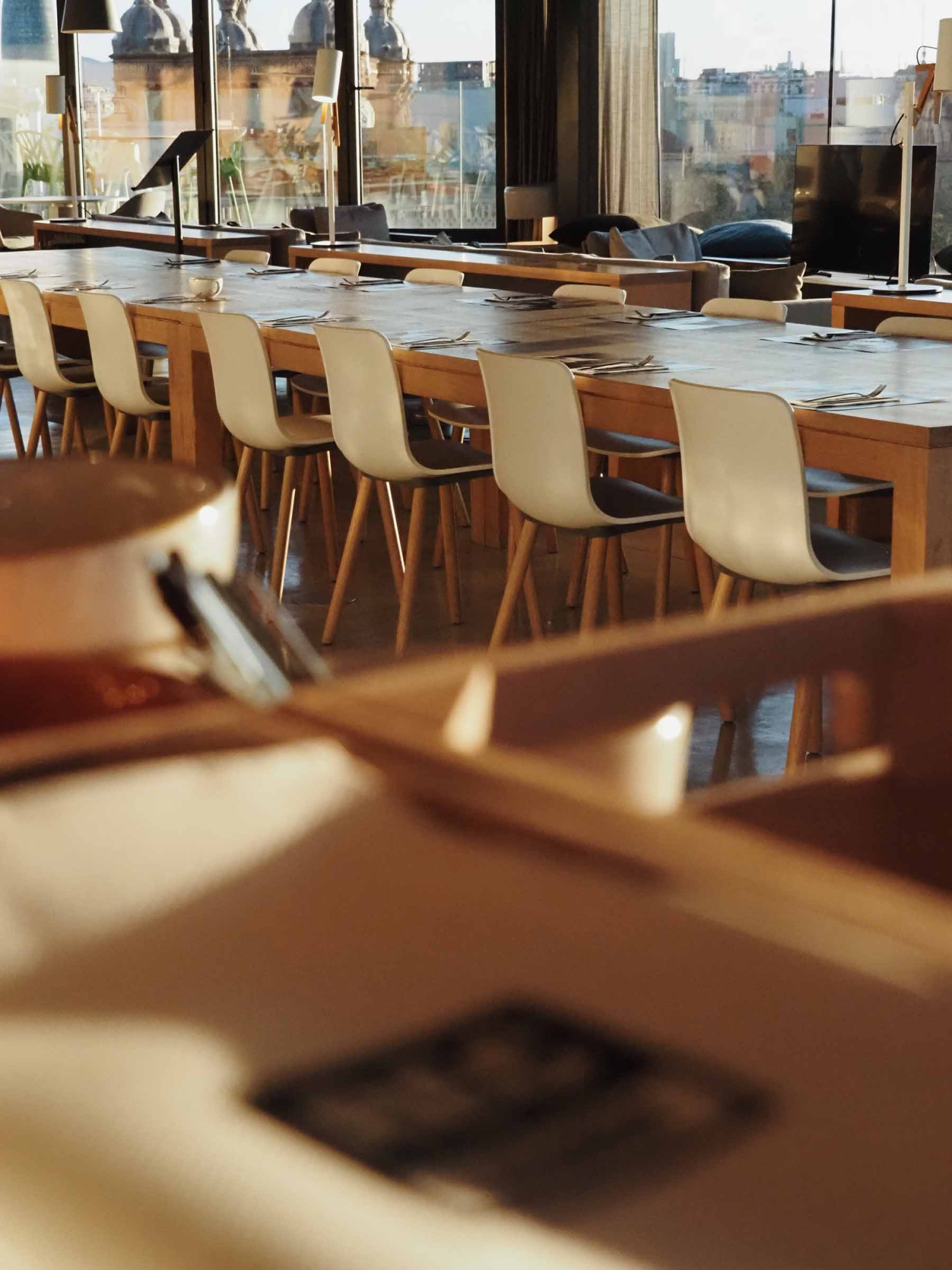 Se ve una sala de reuniones con mesas largas y sillas alrededor, junto a grandes ventanales.