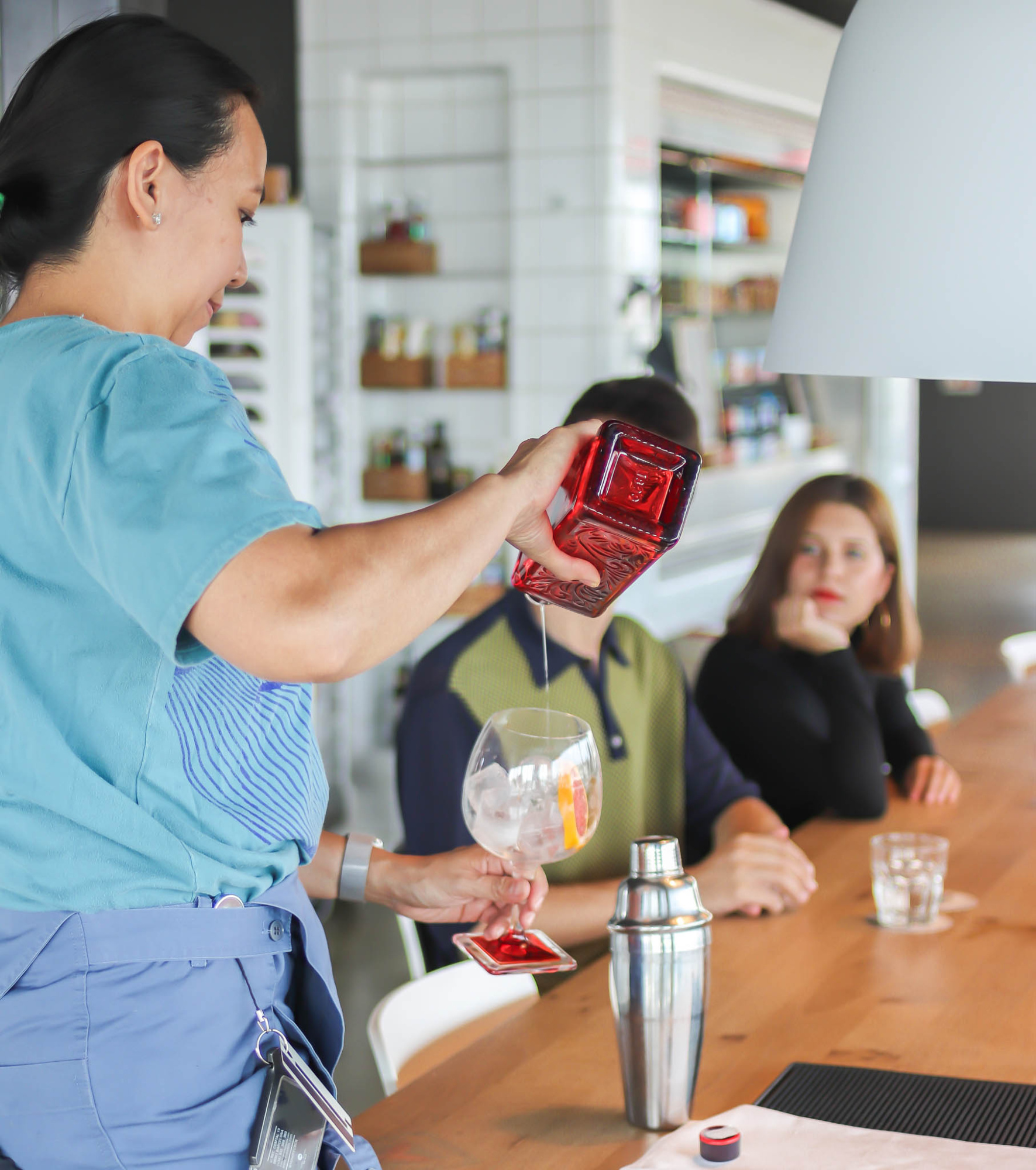 Una camarera sirve vino en una mesa mientras otras personas conversan en un restaurante.