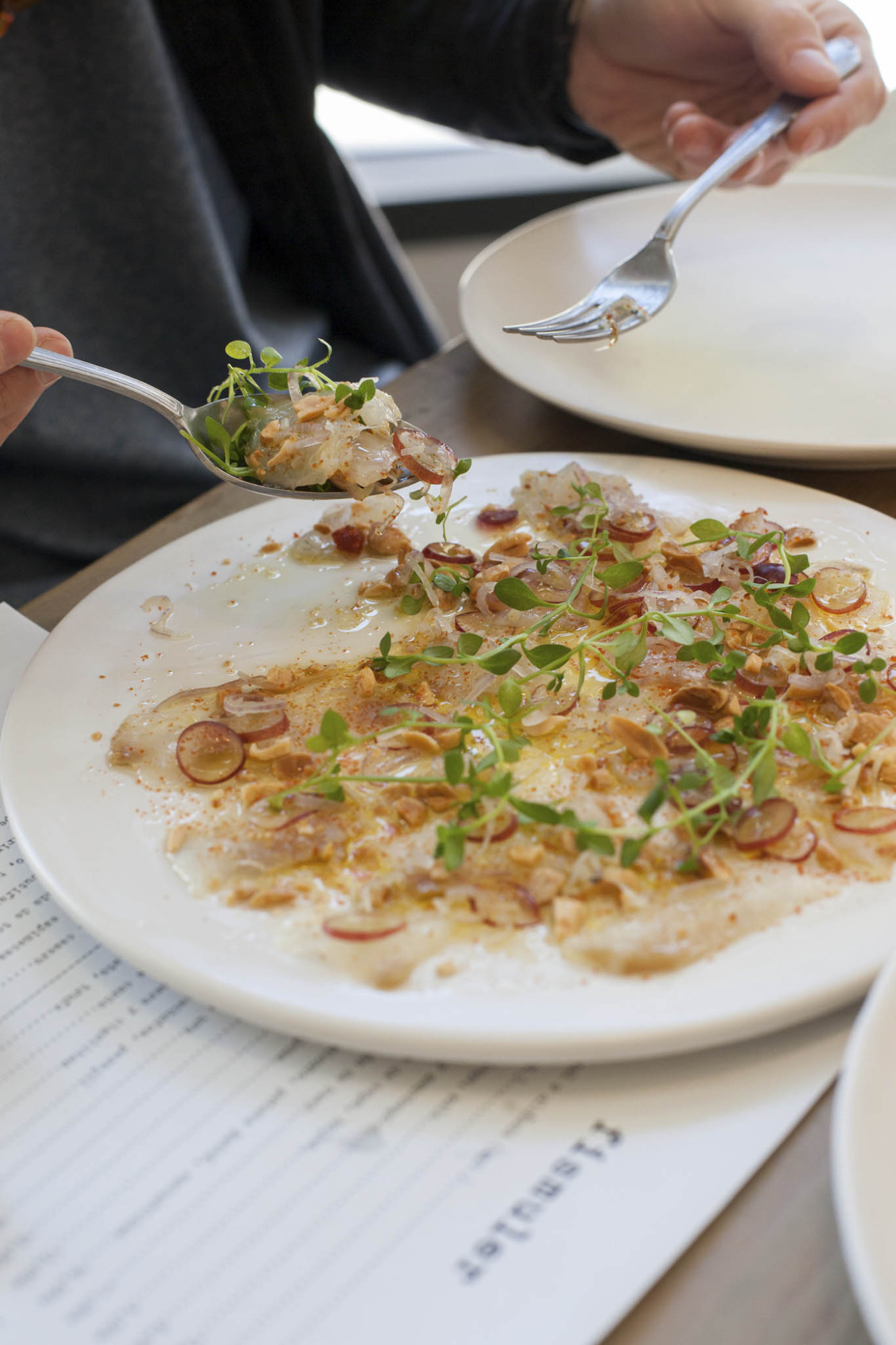 Sirven un plato de pasta con hierbas y trozos de carne en una mesa de restaurante.