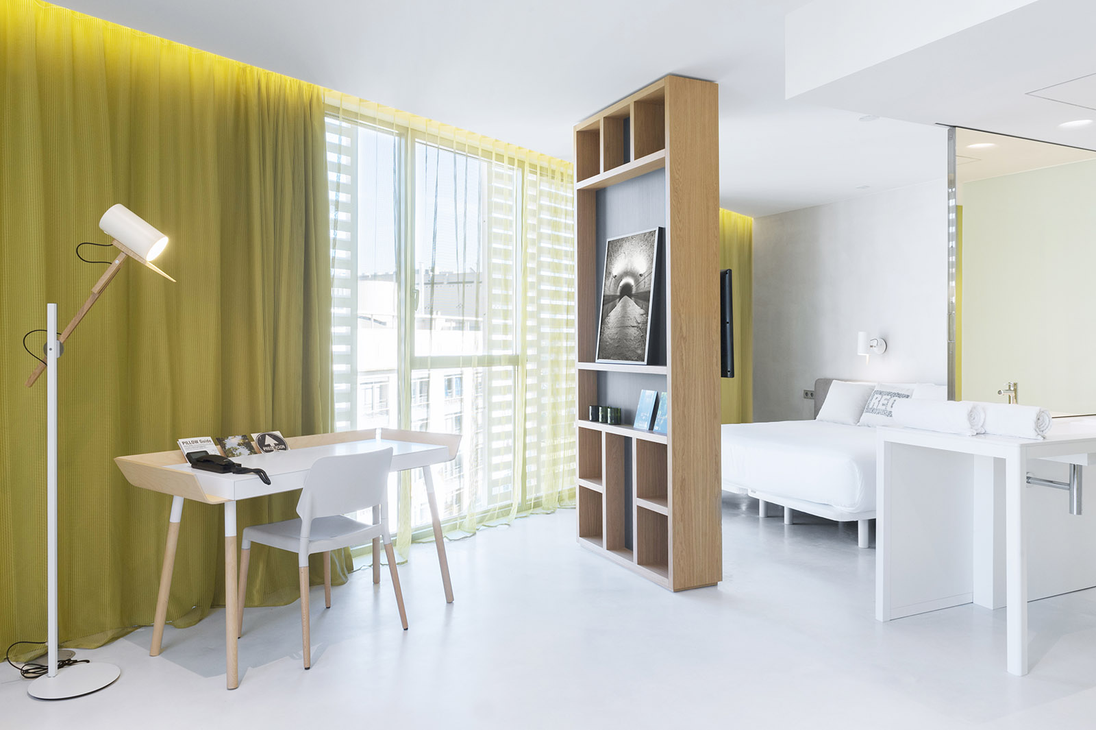 Se ve una suite con mesa, sillas, lámparas de pie y una zona de descanso con cama y estantería.