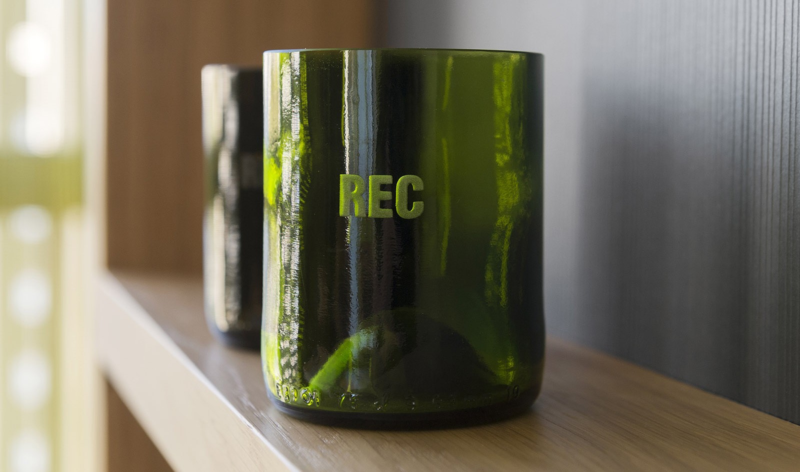 Un jarrón verde con reflejos está sobre una mesa de madera junto a una pared gris.