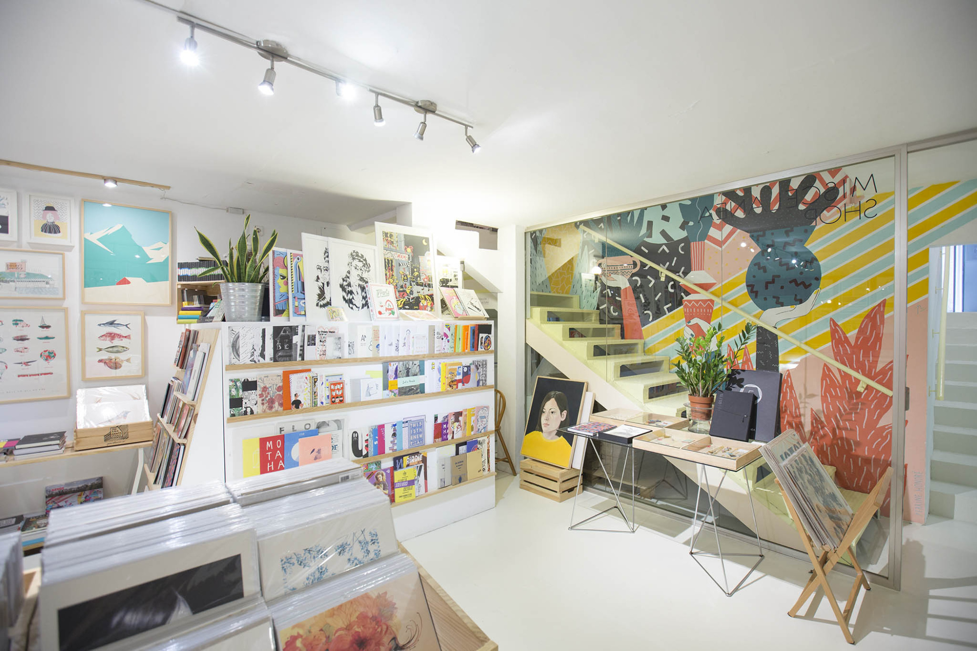 Se ve una zona interior con estanterías, mostrador y sillas junto a una pared decorada.