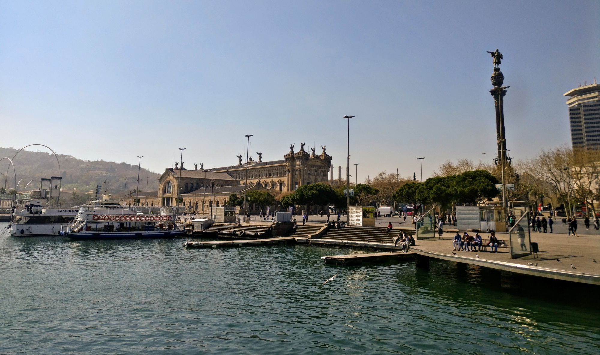 Se ve un paseo marítimo con muelle, barcos y edificios junto al agua.
