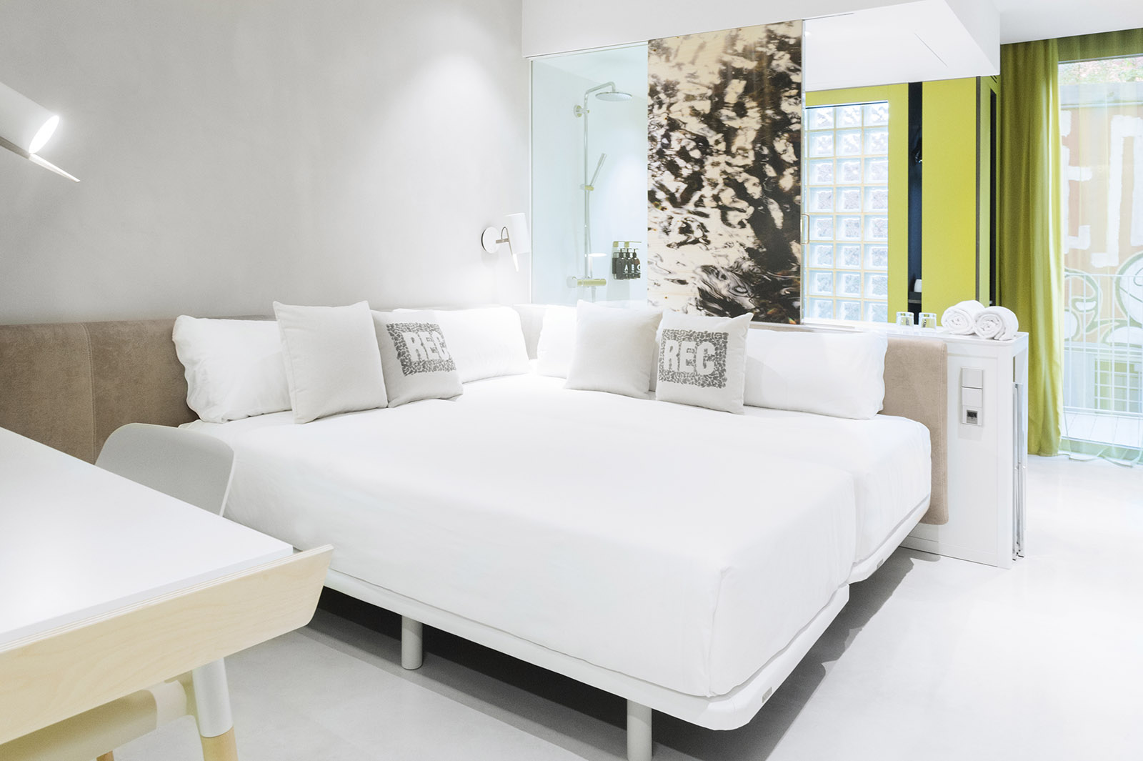 La imagen muestra una cama doble blanca con almohadas y una ventana con cortinas verdes.