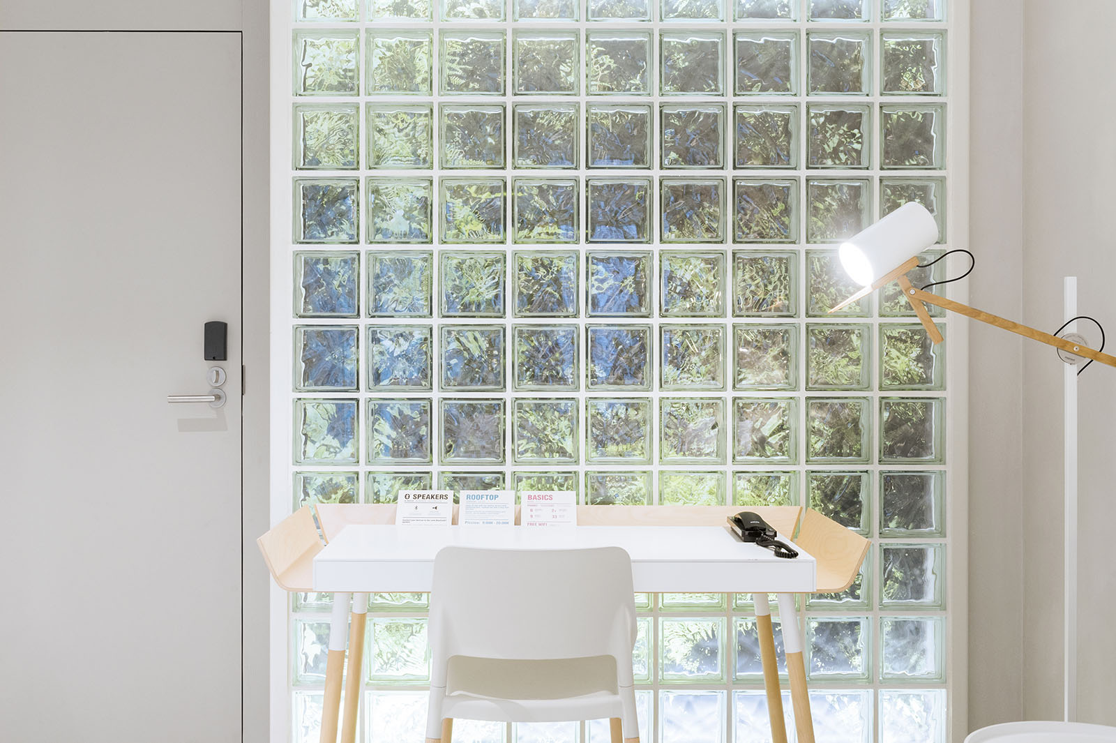 Se ve una mesa alta con dos taburetes y una lámpara sobre una pared con bloques de vidrio.