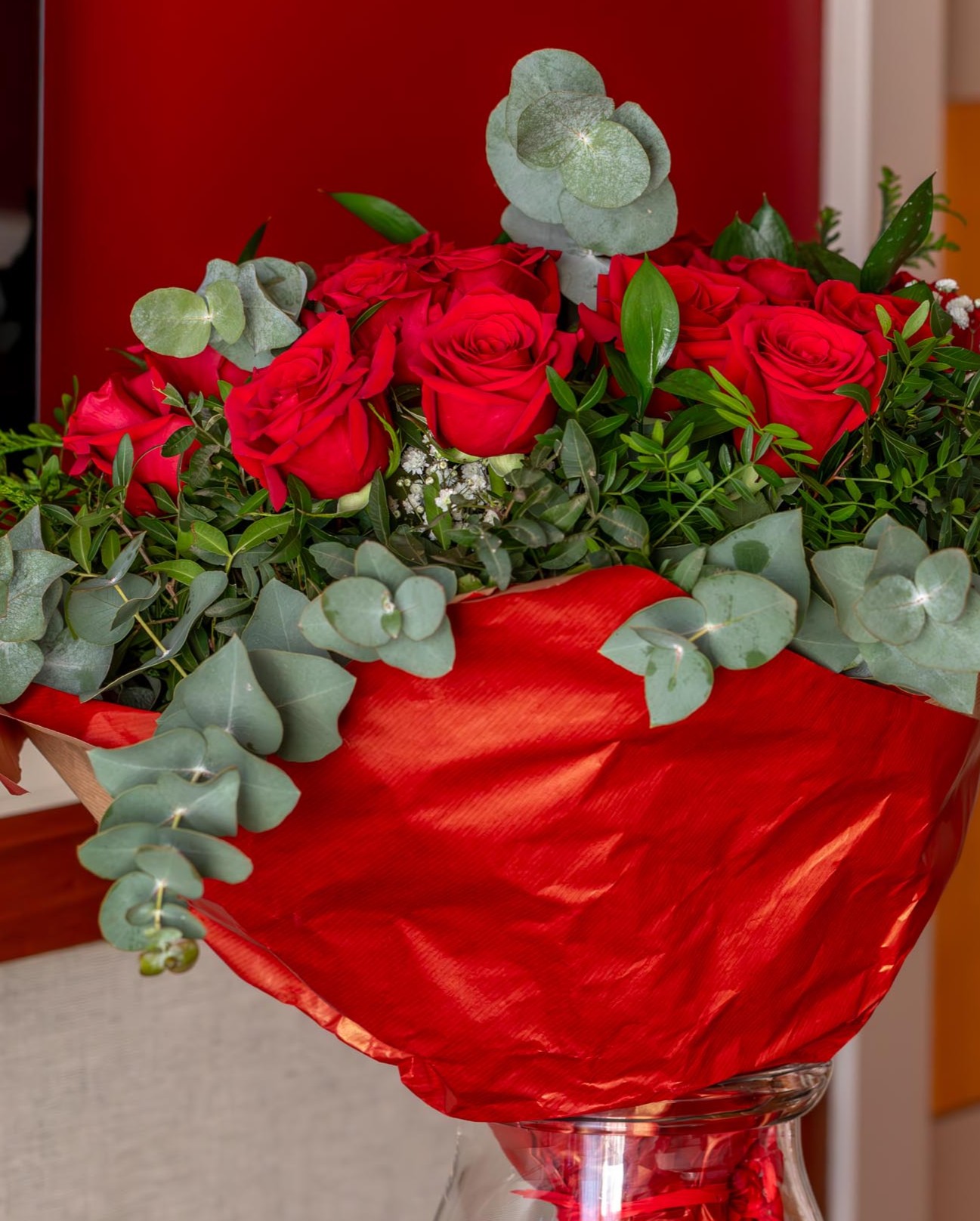 Un ramo de rosas rojas con hojas verdes se muestra en un jarrón de vidrio sobre una mesa.