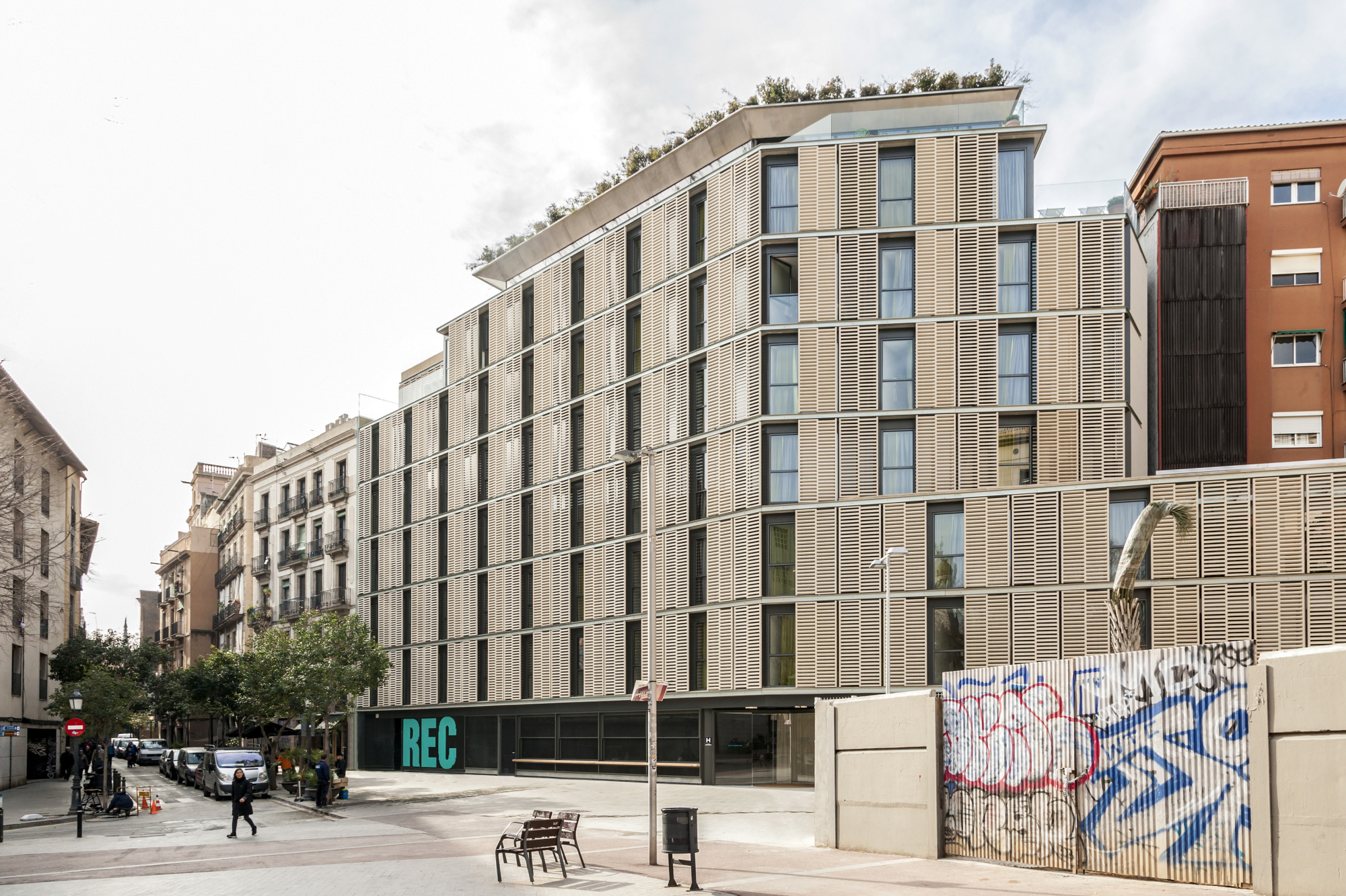 Se ve la fachada de un edificio moderno en una calle urbana con un muro y bicicletas estacionadas.
