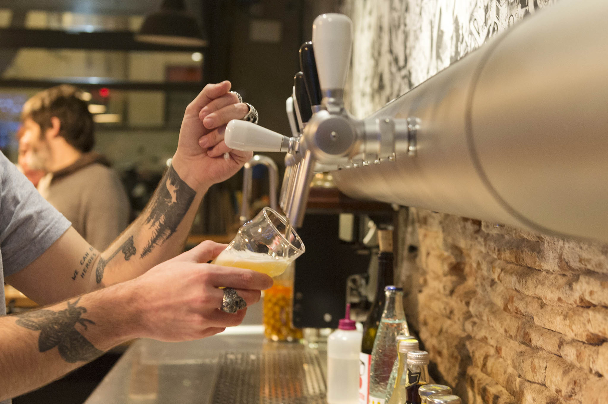 Una persona sirve cerveza desde un grifo sobre una barra con vasos y botellas.