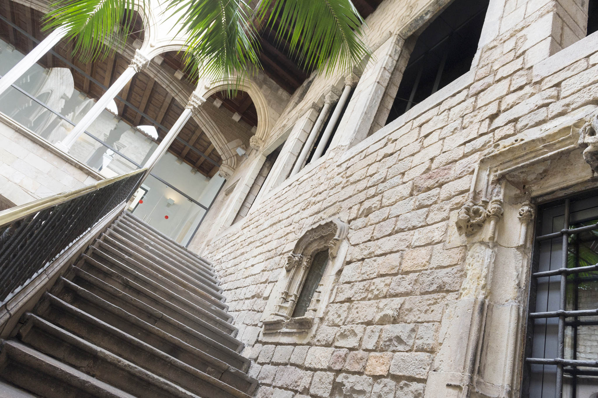 Se ve un patio interior con escaleras, muros de piedra y una ventana con rejas.