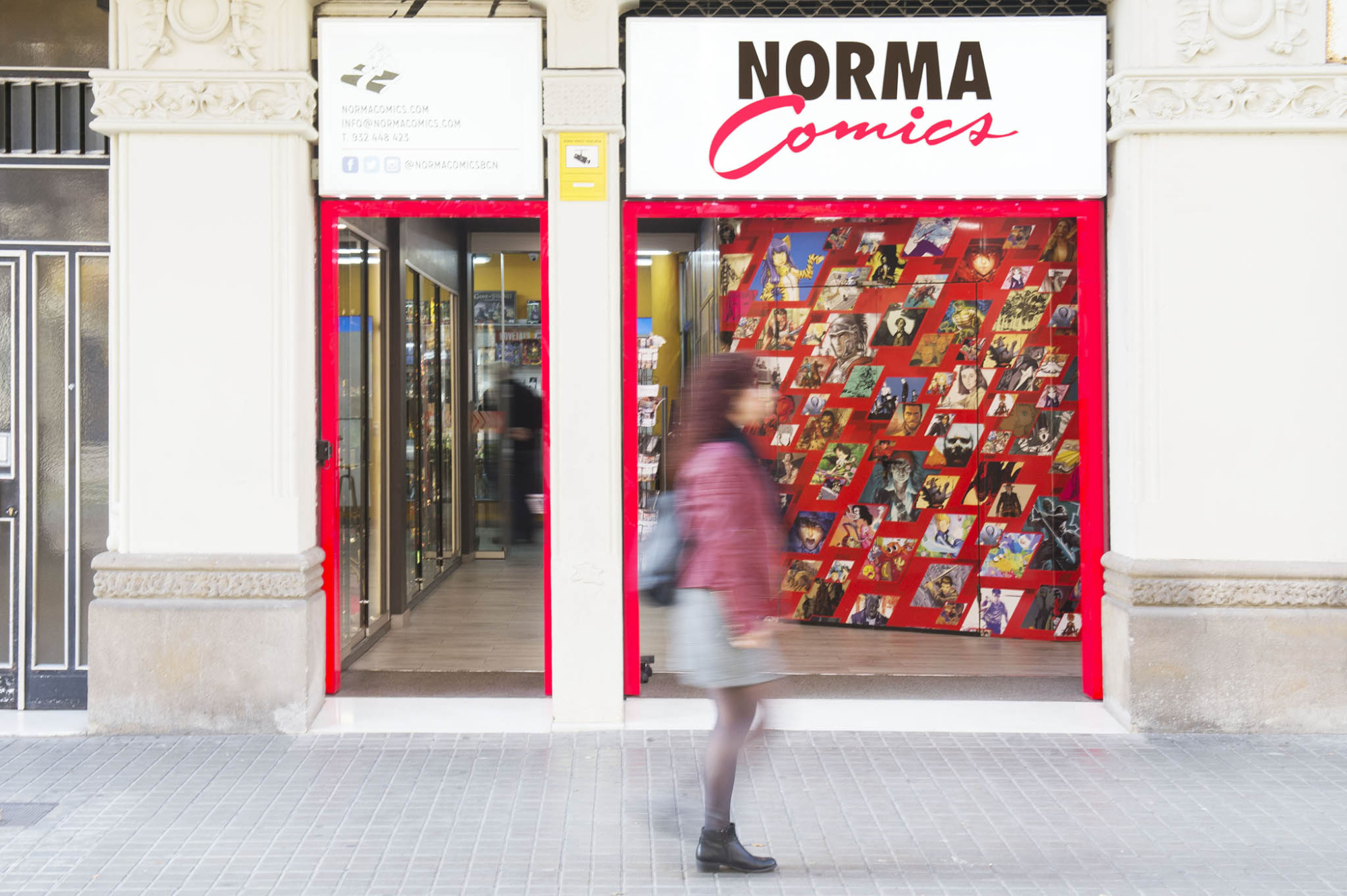Una persona camina frente a una entrada con un escaparate rojo y el letrero “NORMA Comics”.