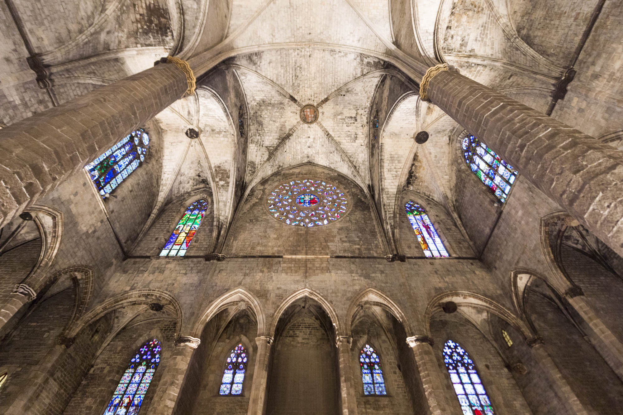Se ve el interior de una iglesia con bóveda de piedra y vitrales en las ventanas altas.