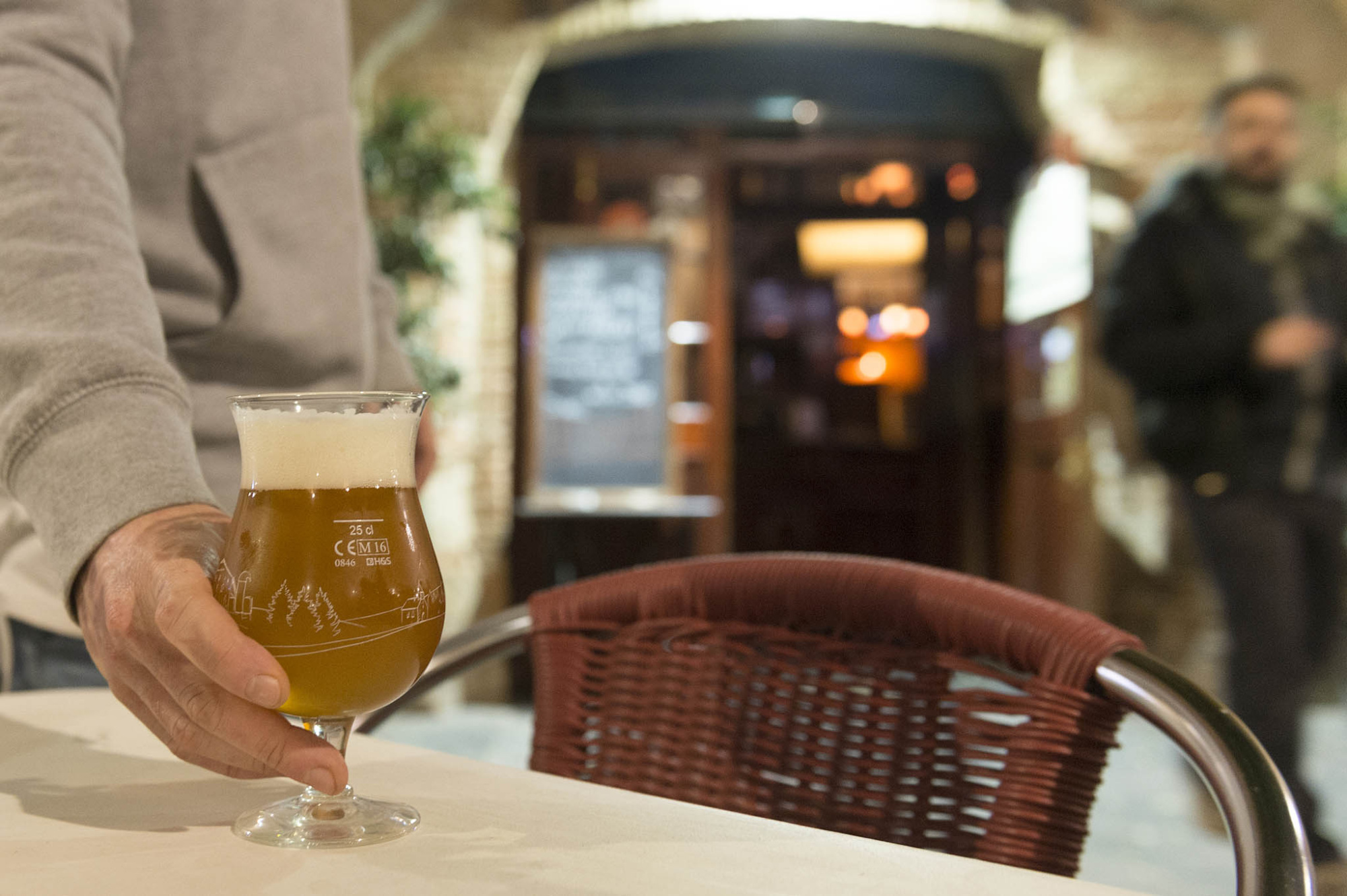 Sirve una copa con bebida sobre una mesa junto a una silla de mimbre en un entorno interior.
