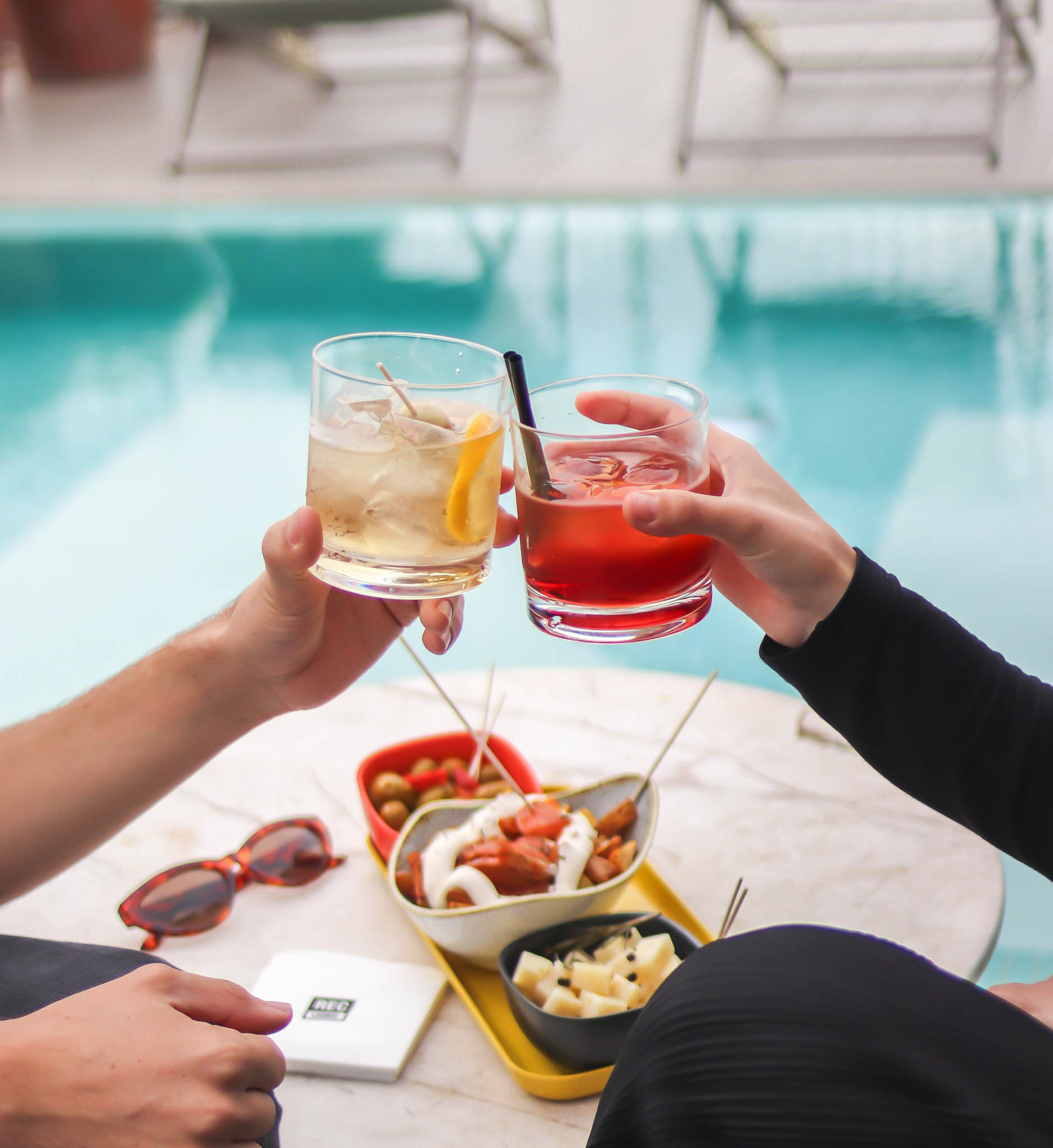 Se brindan con dos vasos de bebida junto a una piscina al aire libre.