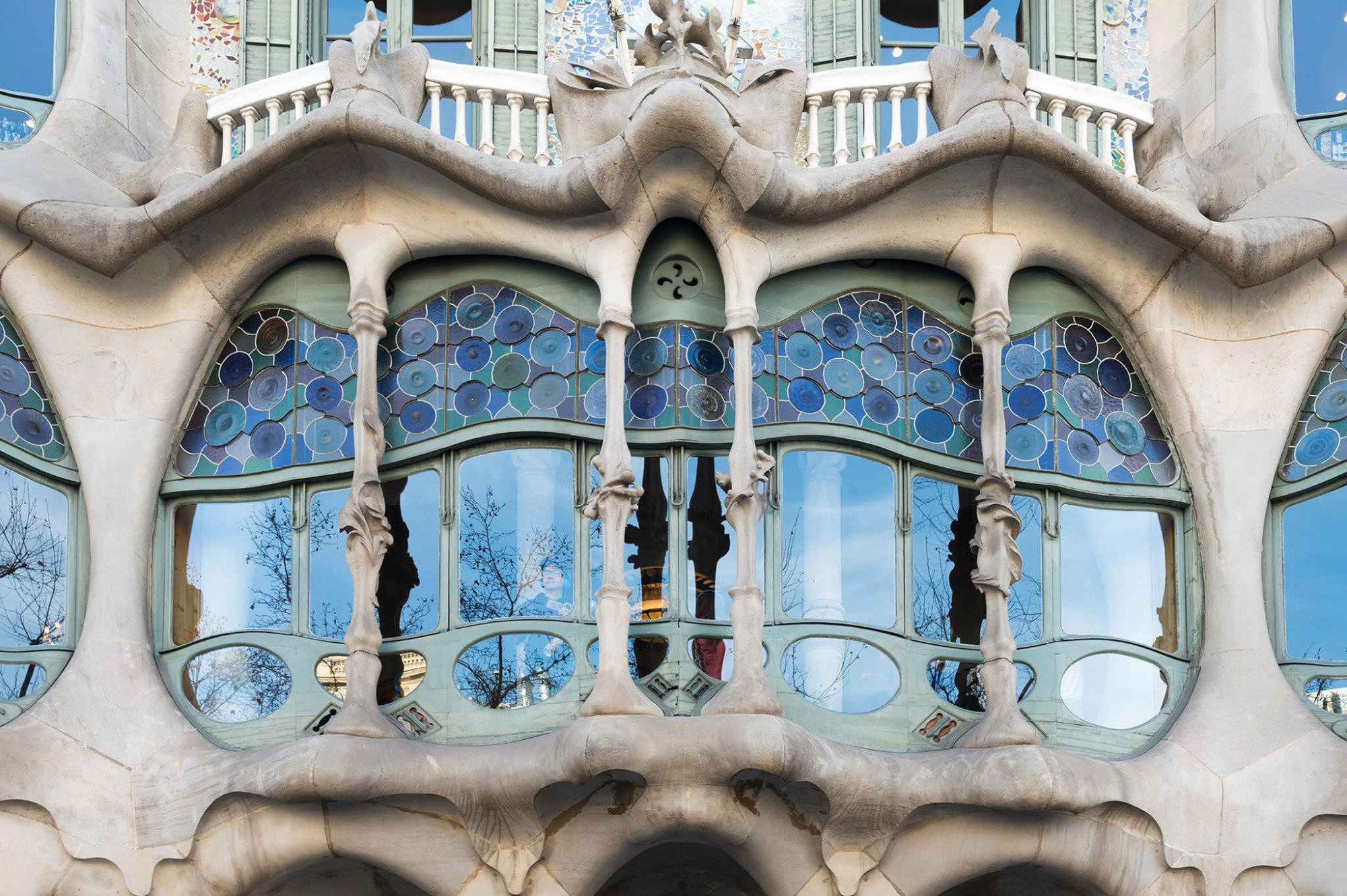 Si vede una facciata modernista con archi in pietra, colonne e finestre decorate con mosaici blu.