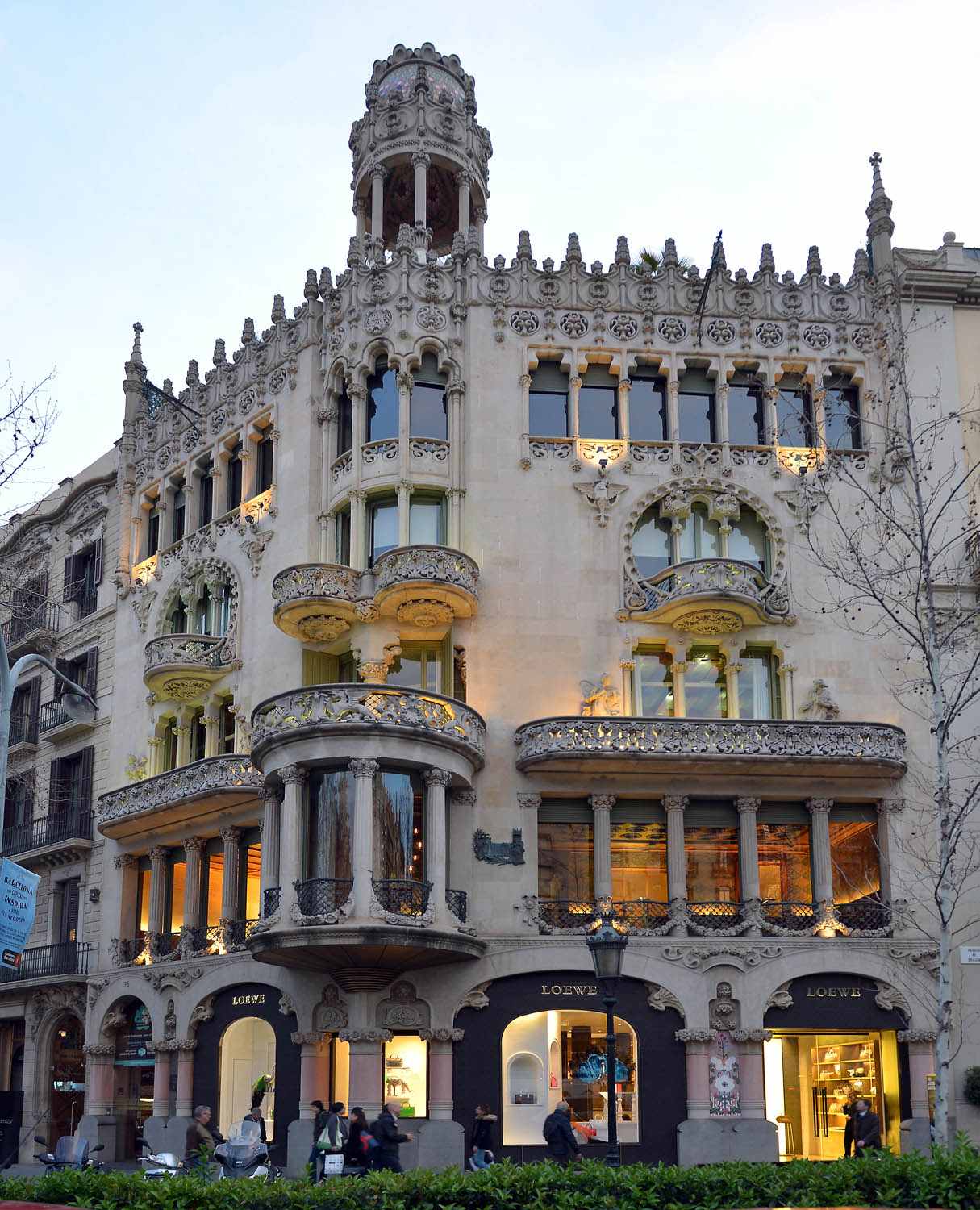 Si vede una facciata modernista con balconi e archi decorativi che si affaccia sulla strada.