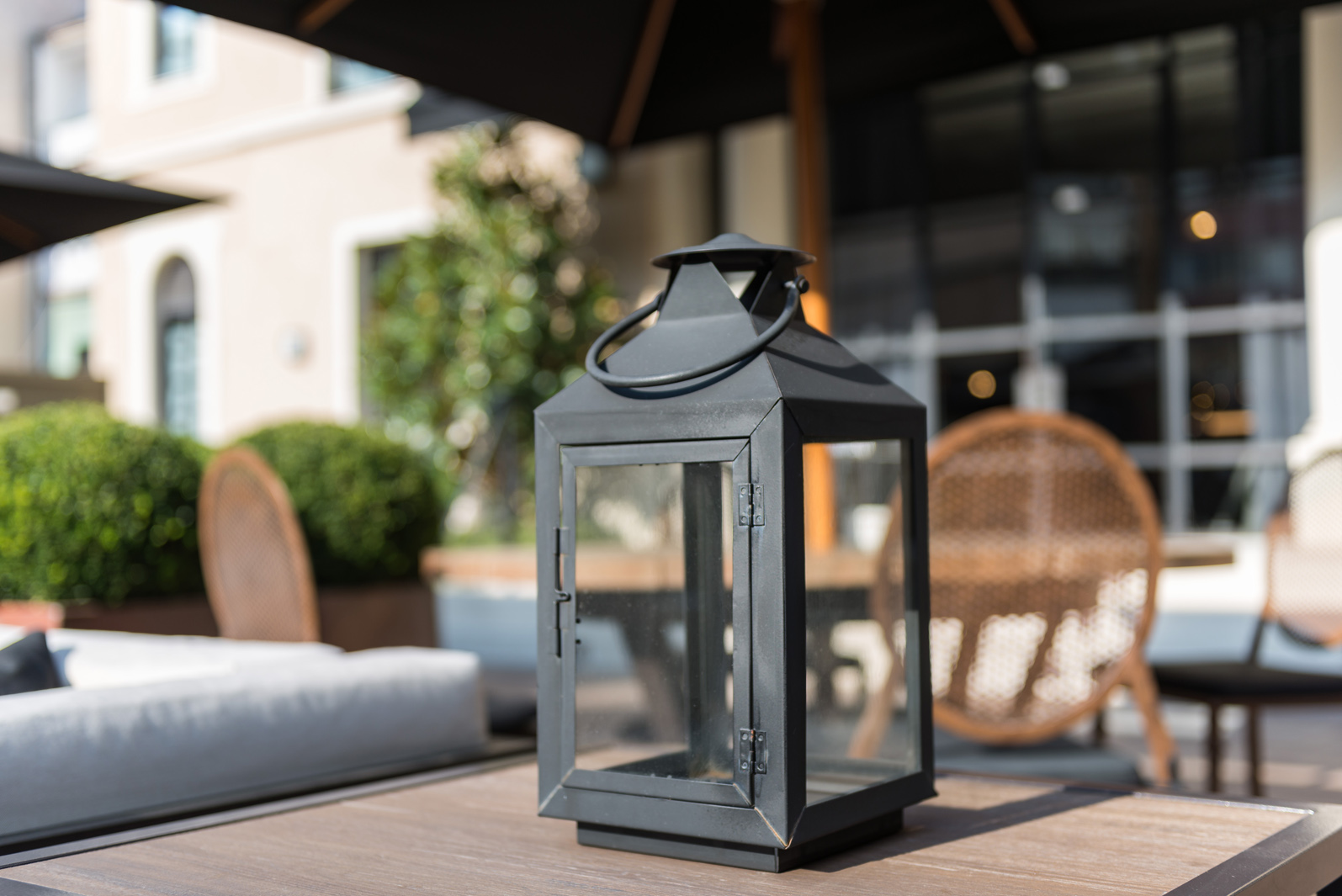 Se ve una linterna decorativa sobre una mesa de madera en una terraza con asientos al fondo.