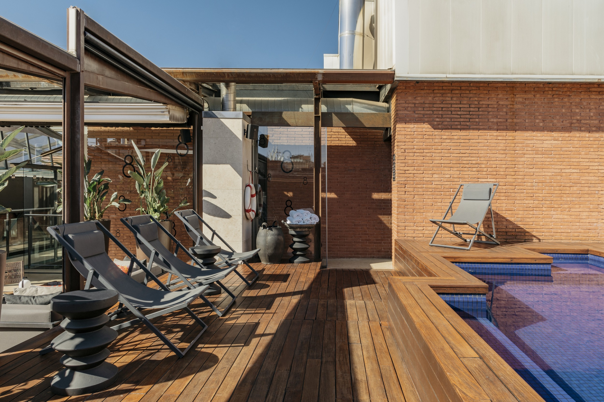Se ve una terraza con tumbonas, una piscina rectangular y suelo de madera junto a paredes de ladrillo.