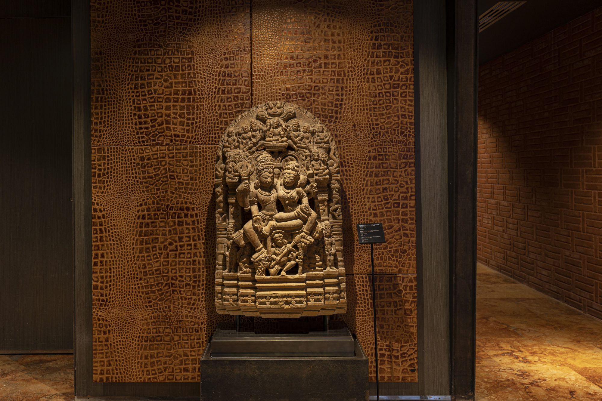 Se ve una escultura decorativa sobre un pedestal en un pasillo con paredes de ladrillo y luz cálida.