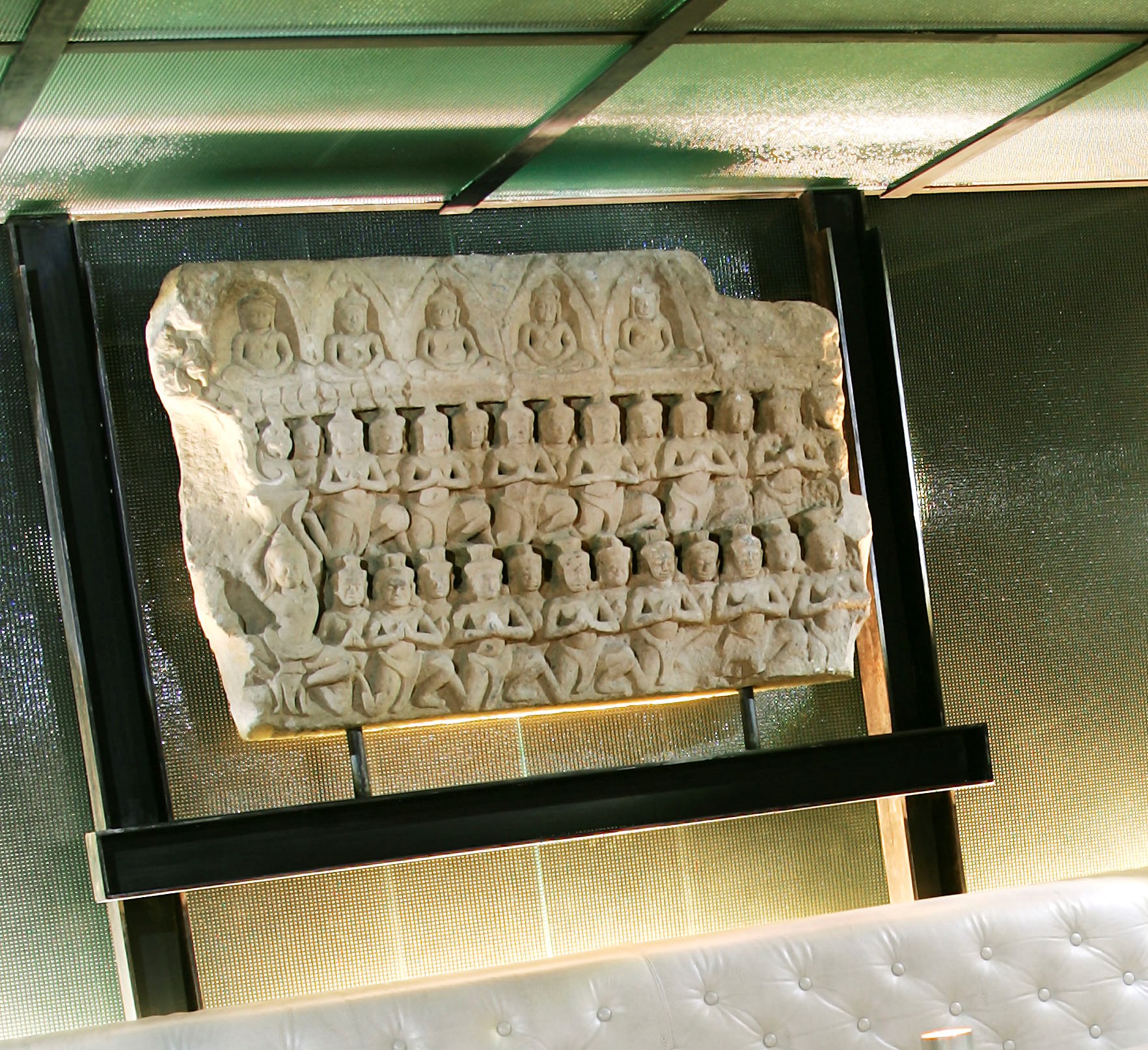 Se ve un relieve escultórico de estilo antiguo dentro de una vitrina con soporte metálico.