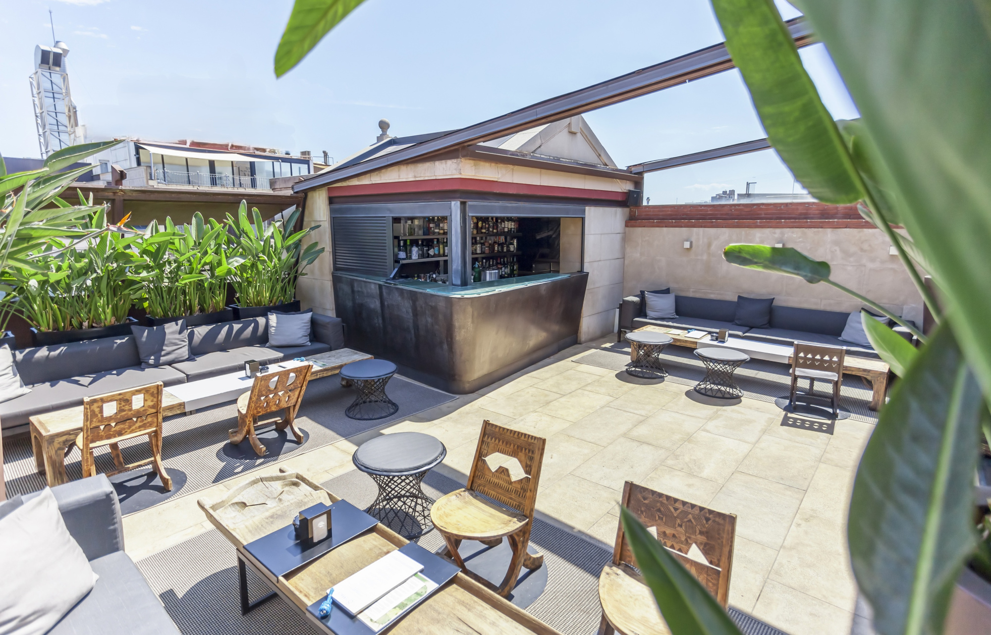 Se ve una terraza exterior con mesas y sillas, una zona de barbacoa y plantas alrededor.