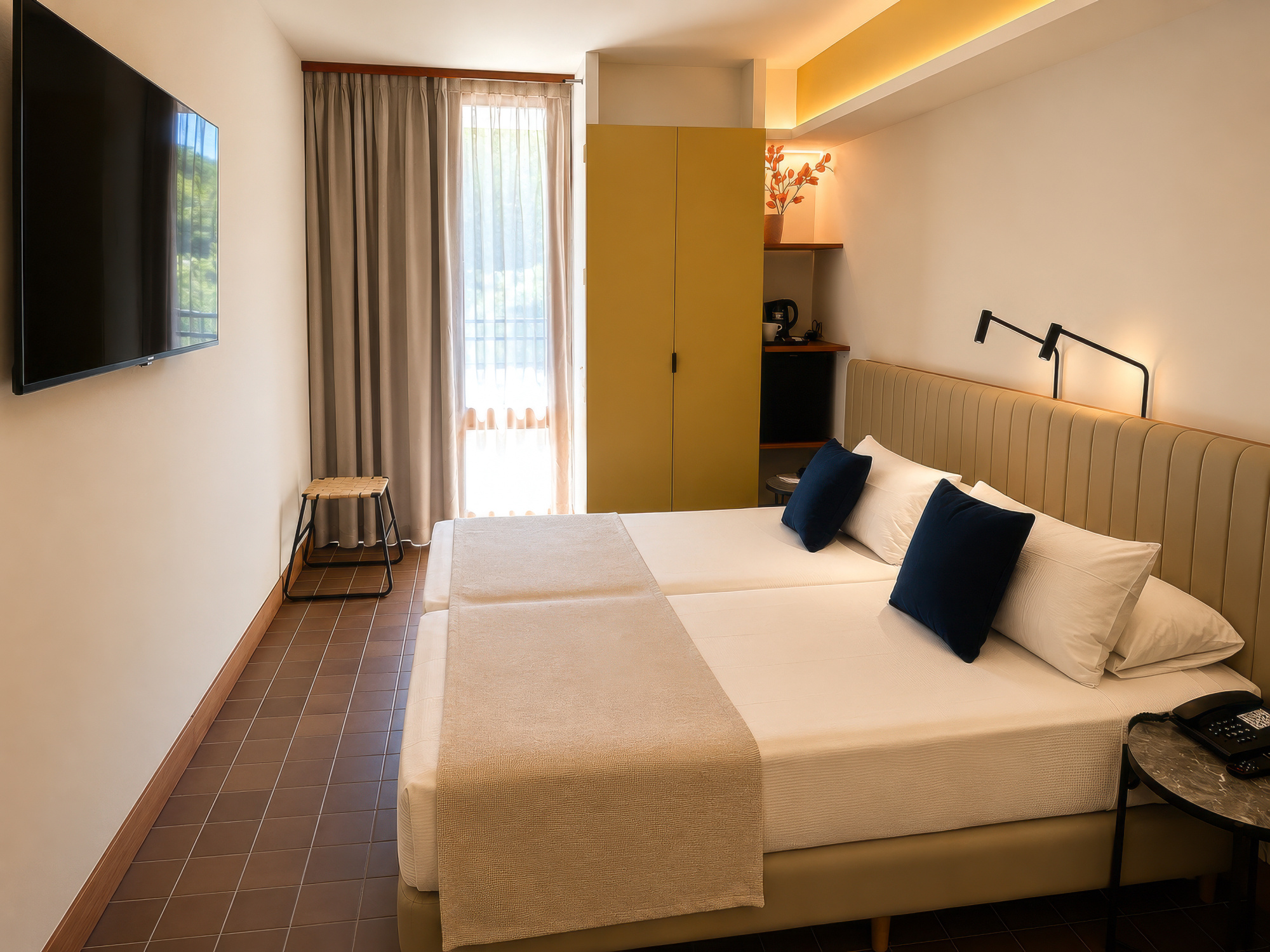 Describe una cama doble con almohadas en una habitación luminosa con armario y cortinas.