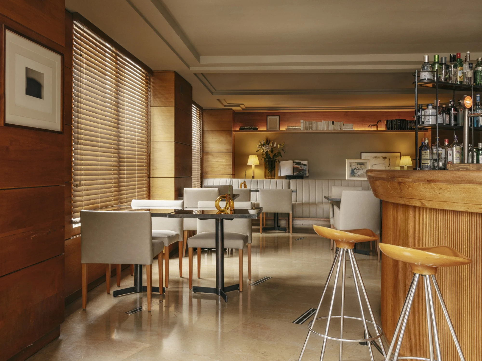 Se ve un bar interior con taburetes altos, mesas y sillas junto a una barra de madera.