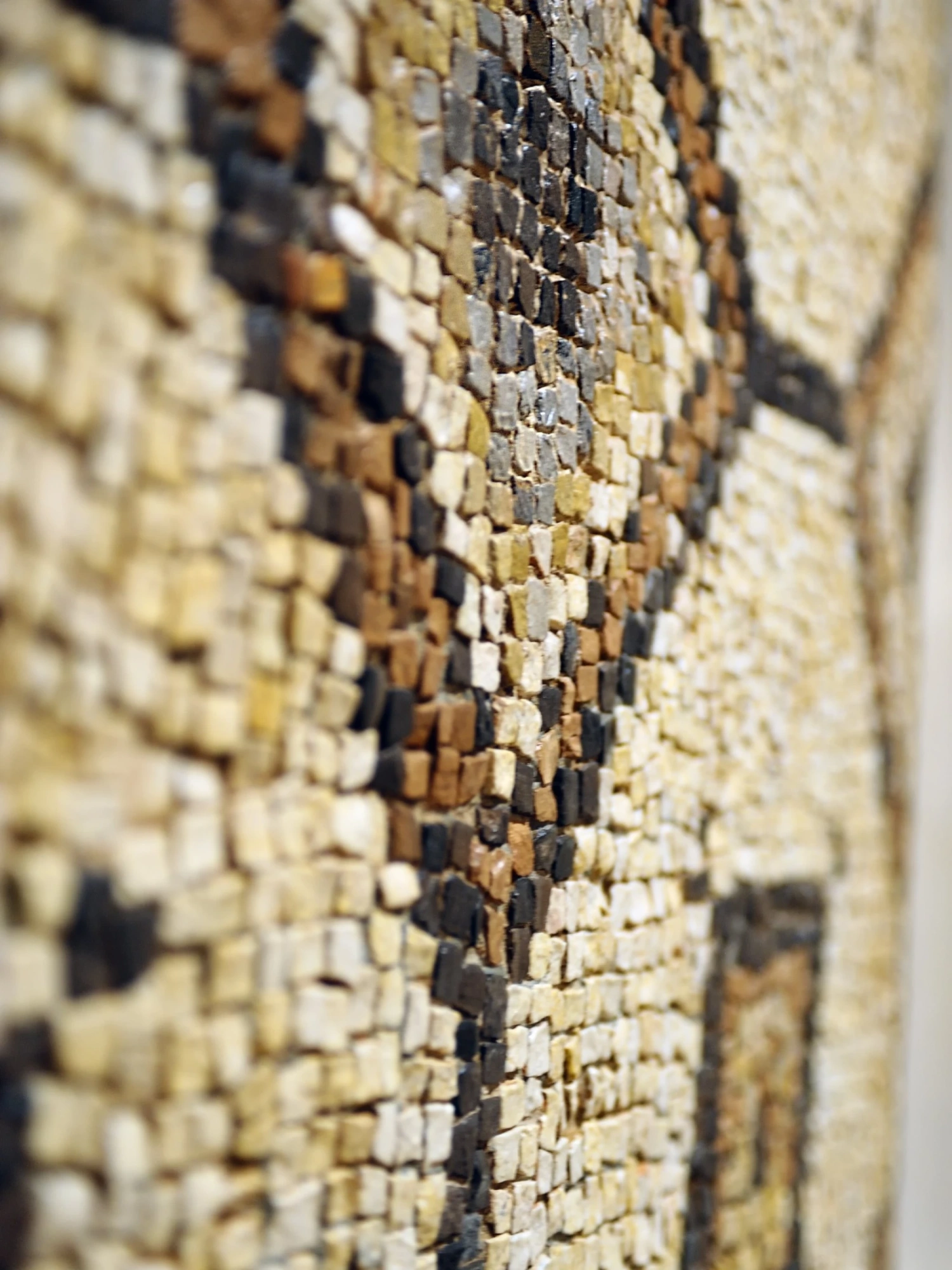 Se ve un mosaico decorativo con pequeñas piezas en tonos dorados y beige dispuestas en una pared.
