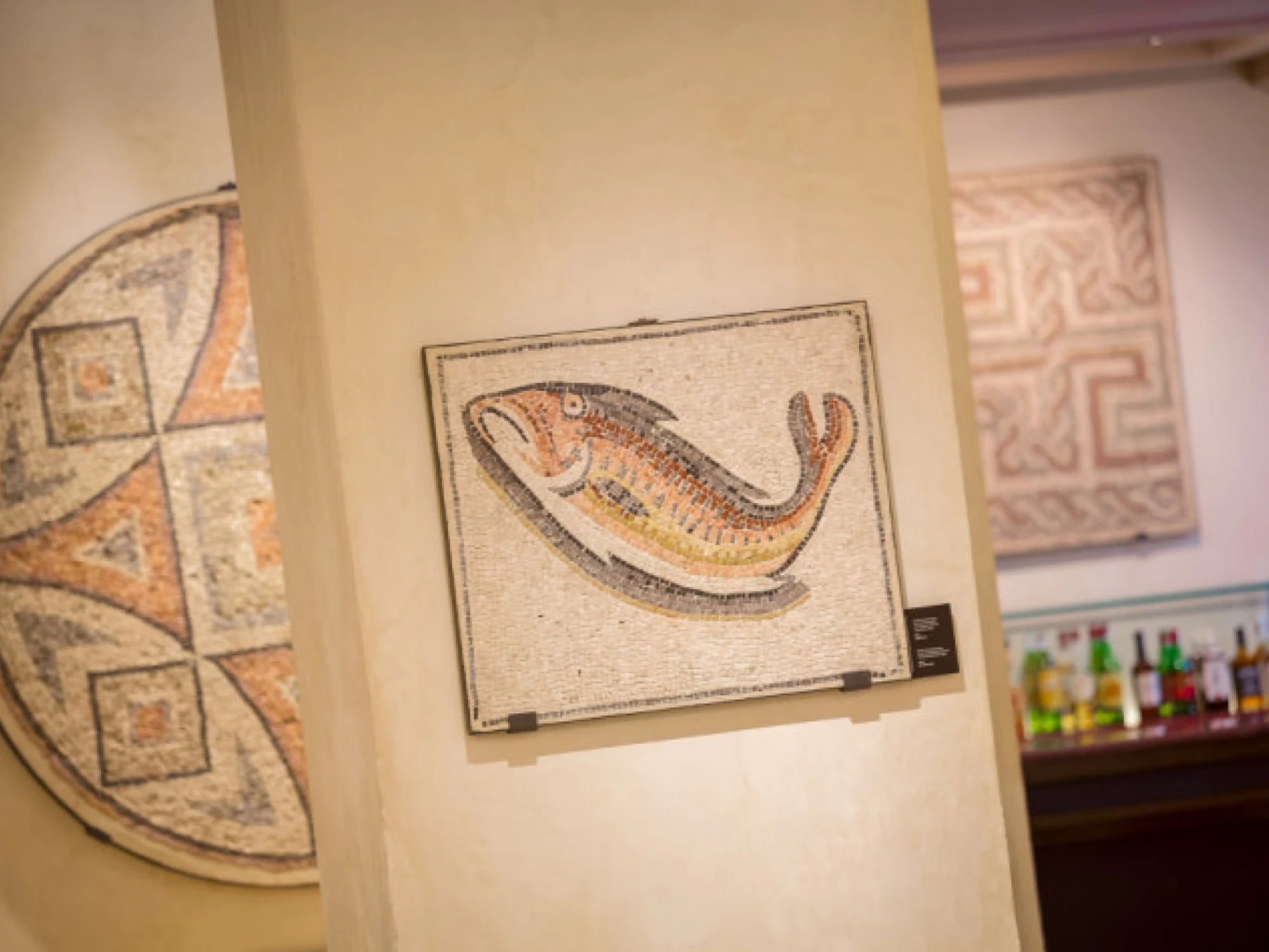 Se ve un mosaico decorativo con forma de pez en una pared, junto a otras piezas de arte en el interior.