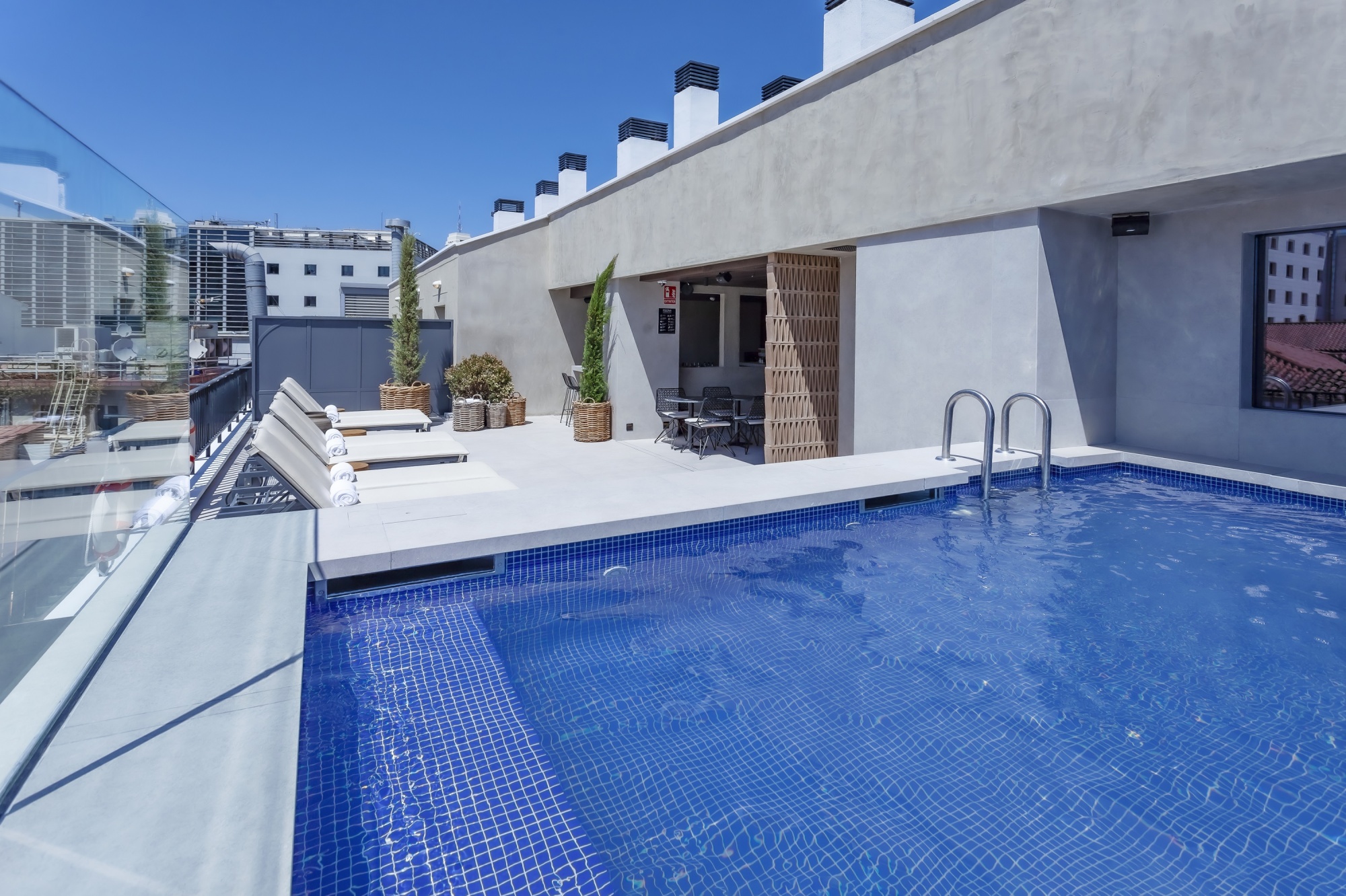 Se ve una piscina azul en una terraza de azotea con barandillas y paredes claras alrededor.