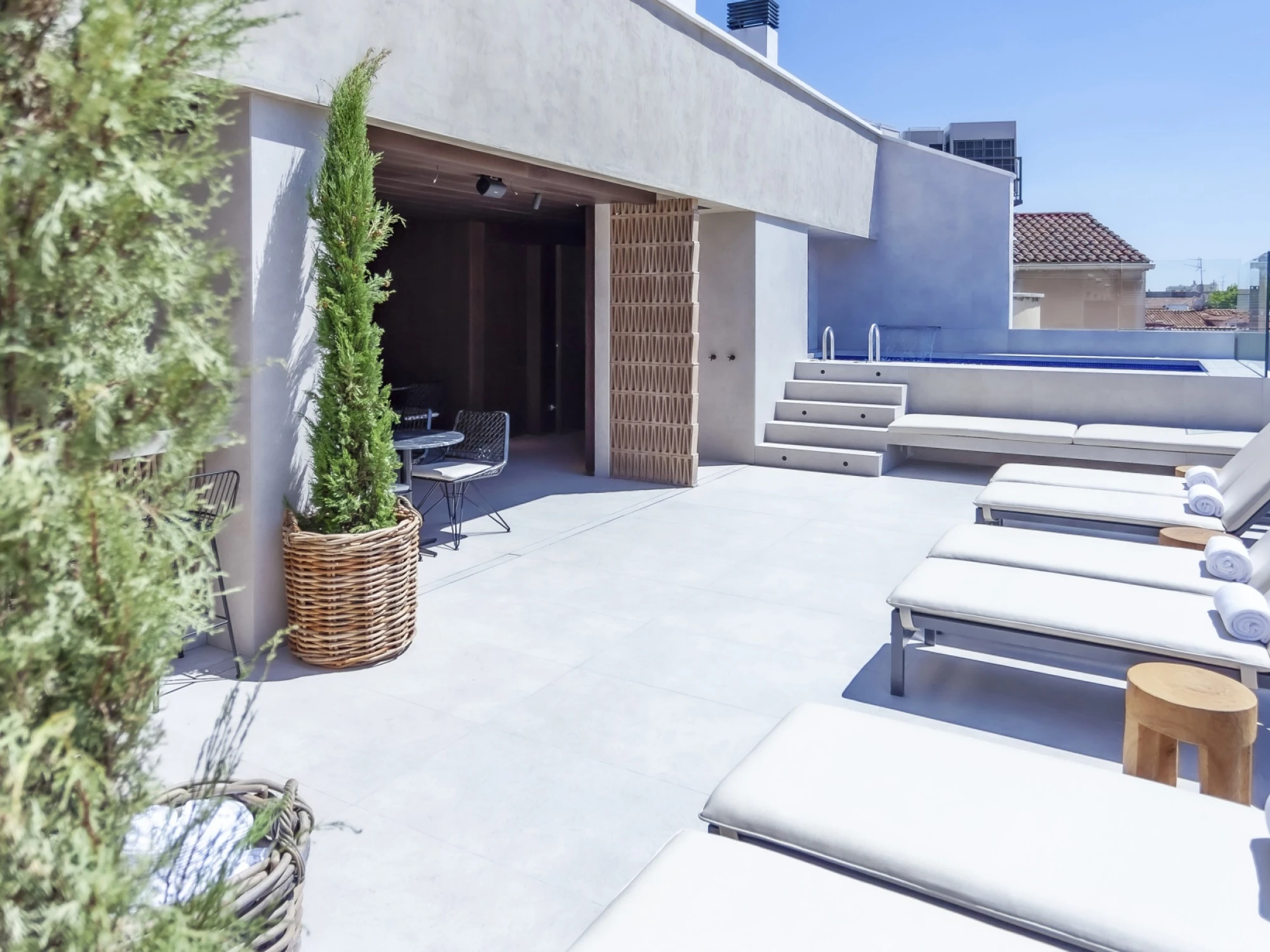 Se ve una terraza exterior con tumbonas, bancos y una zona de descanso junto a una pared blanca.