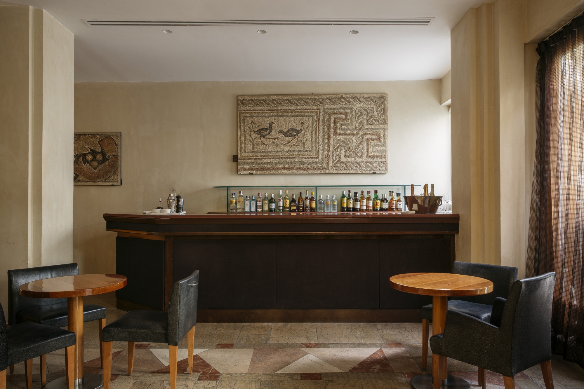 Se ve una barra de bar de madera con botellas y varios asientos alrededor en un interior con iluminación tenue.
