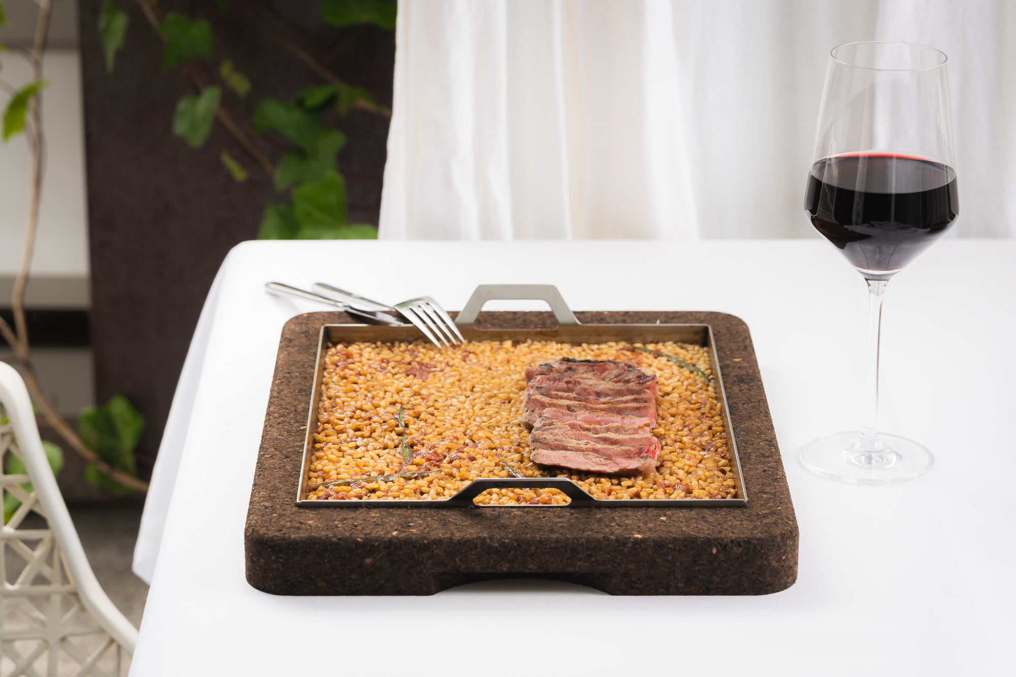 Se ve una mesa con una parrilla de piedra, un vaso de vino y una copa sobre un mantel blanco.