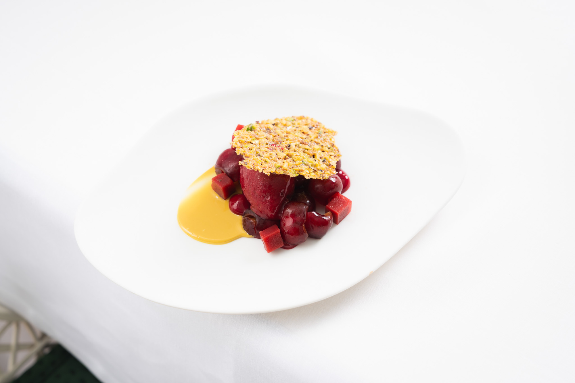 Se ve un plato blanco con un postre decorado sobre una mesa blanca.