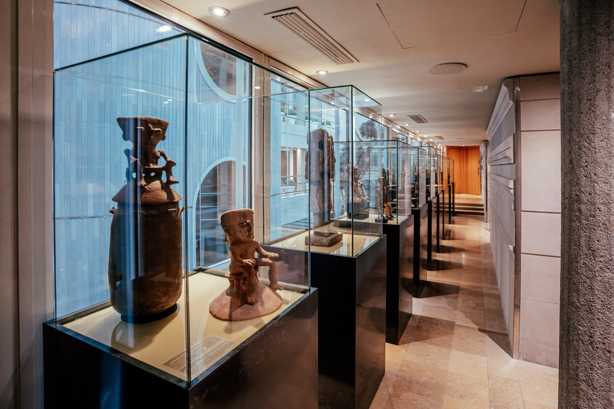 Se ven vitrinas con figuras y objetos decorativos dentro de un pasillo con iluminación empotrada.