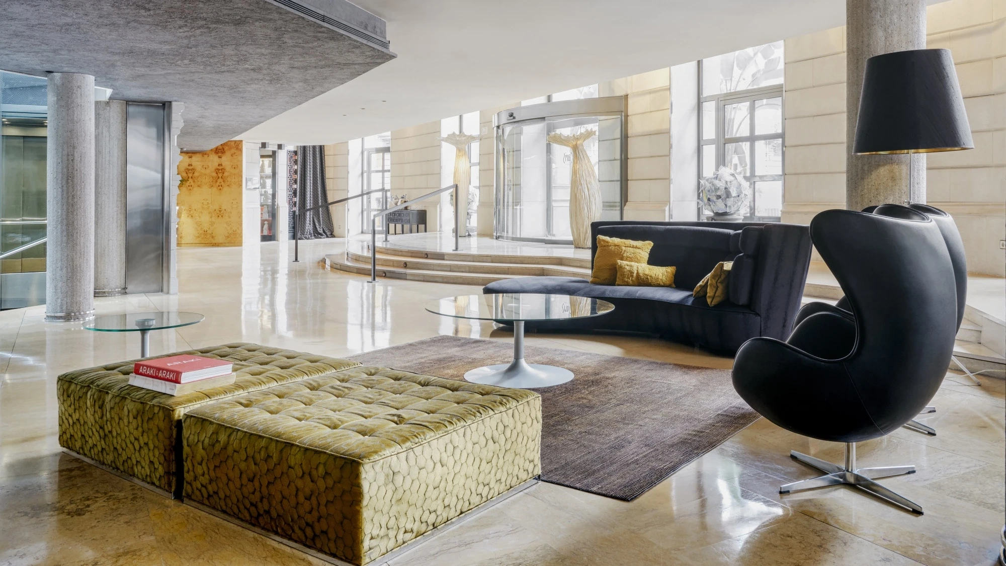 Un amplio vestíbulo con suelo de mármol claro y paredes en tonos neutros, decorado con mobiliario moderno y elegante que invita a la bienvenida y la comodidad.