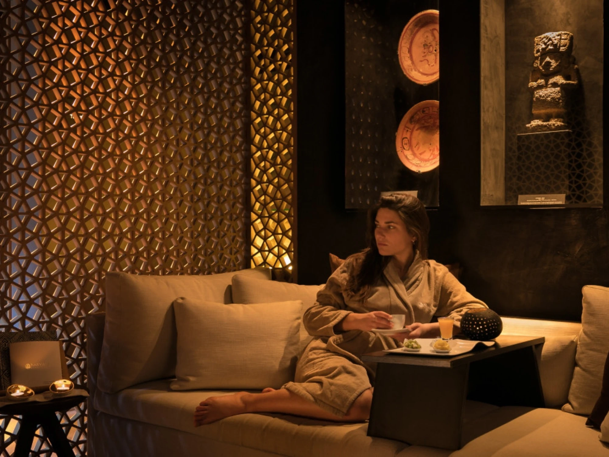 Imagen que muestra un espacio de spa con un ambiente relajante, decorado con tonos cálidos y elementos naturales que evocan la cultura maya.