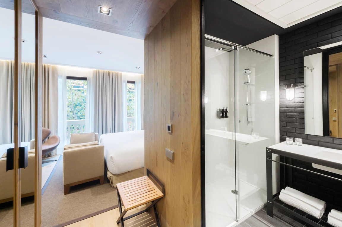 Se ve una zona de estar con sillón y cama, junto a un baño con cabina de ducha y lavabo.
